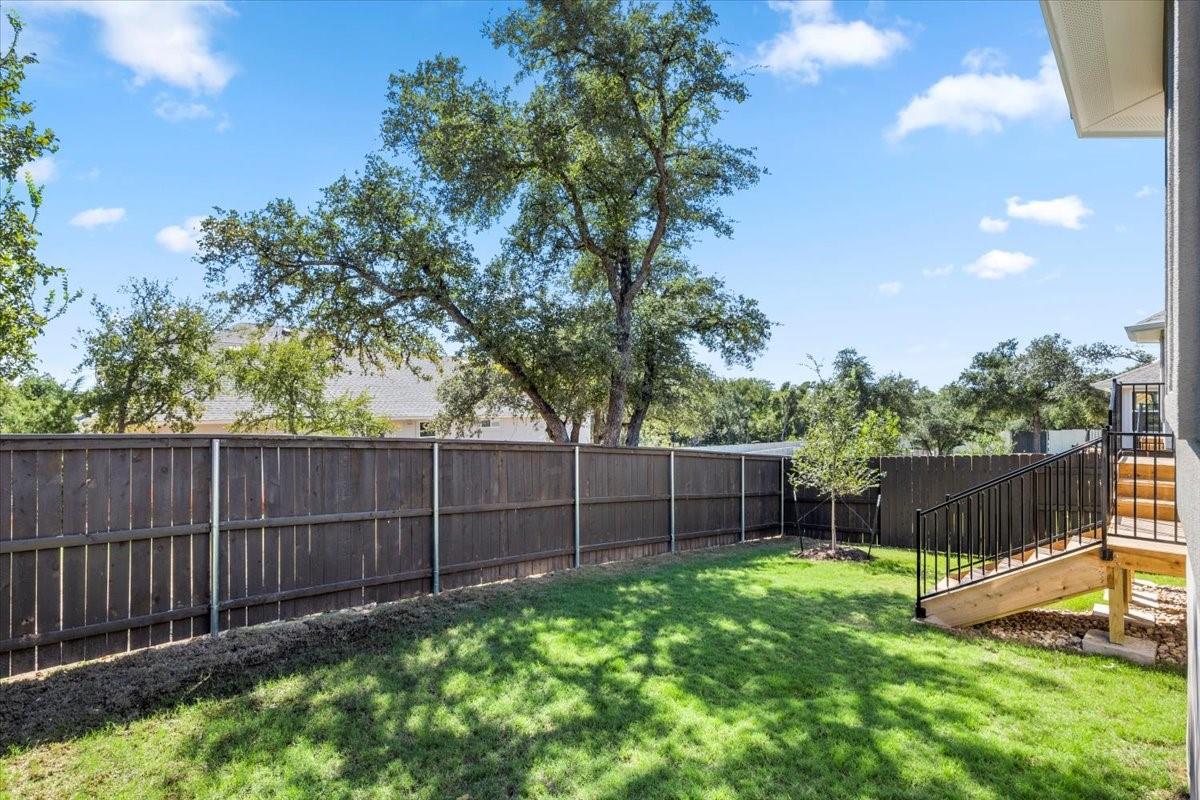 Backyard with a wooden privacy fence, mature oak trees, and stairs leading to a raised deck.