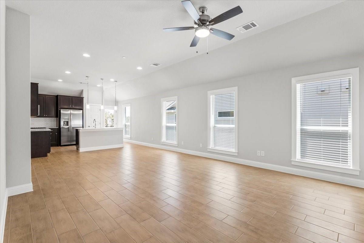 Vacant open-plan living room with tan tile floors, dark kitchen cabinets, and a white island.