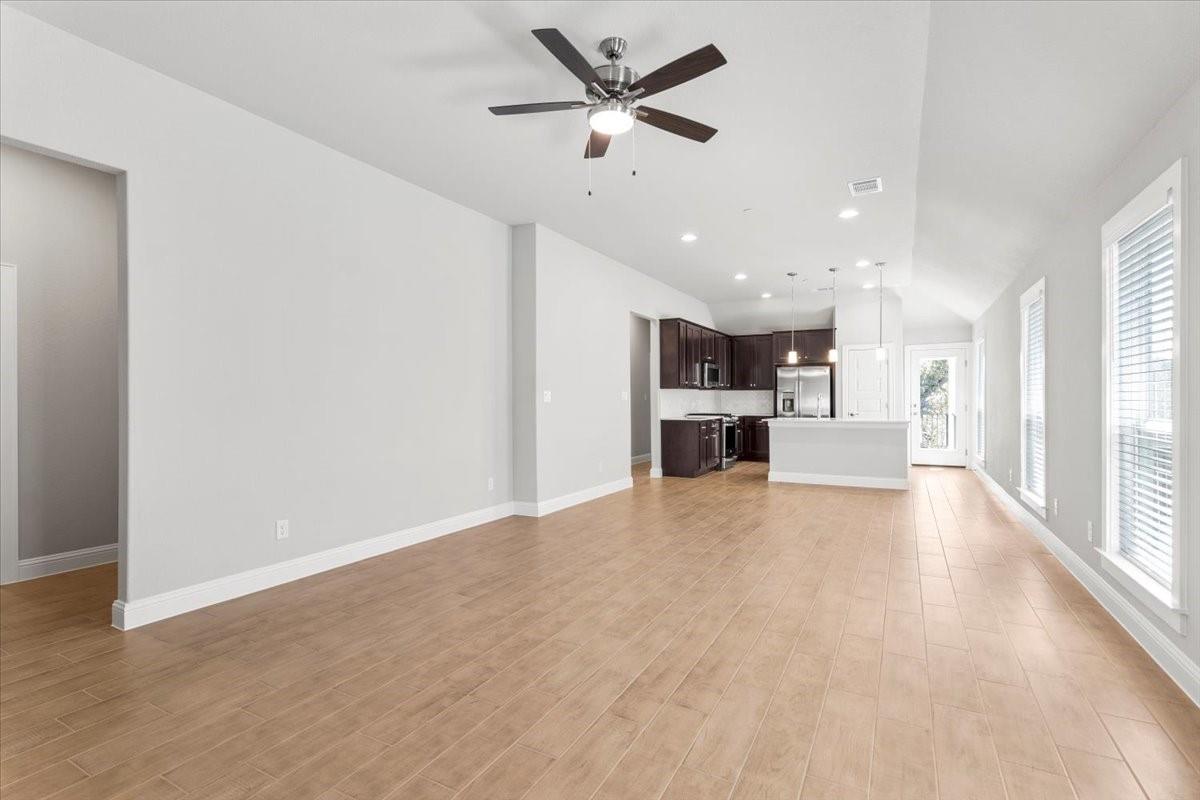 Open living and kitchen area with wood-look tile floors, dark cabinets, and tall windows.