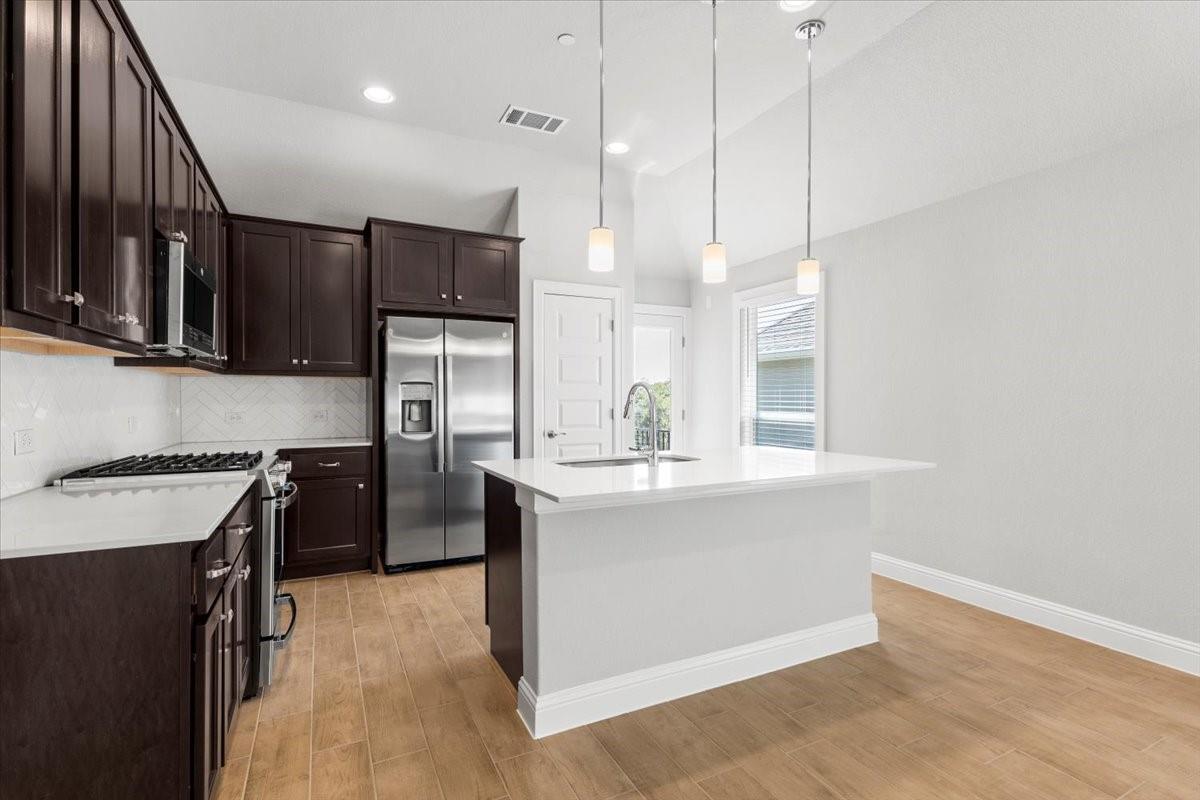 Kitchen with a large white island, dark cabinets, and stainless steel appliances.