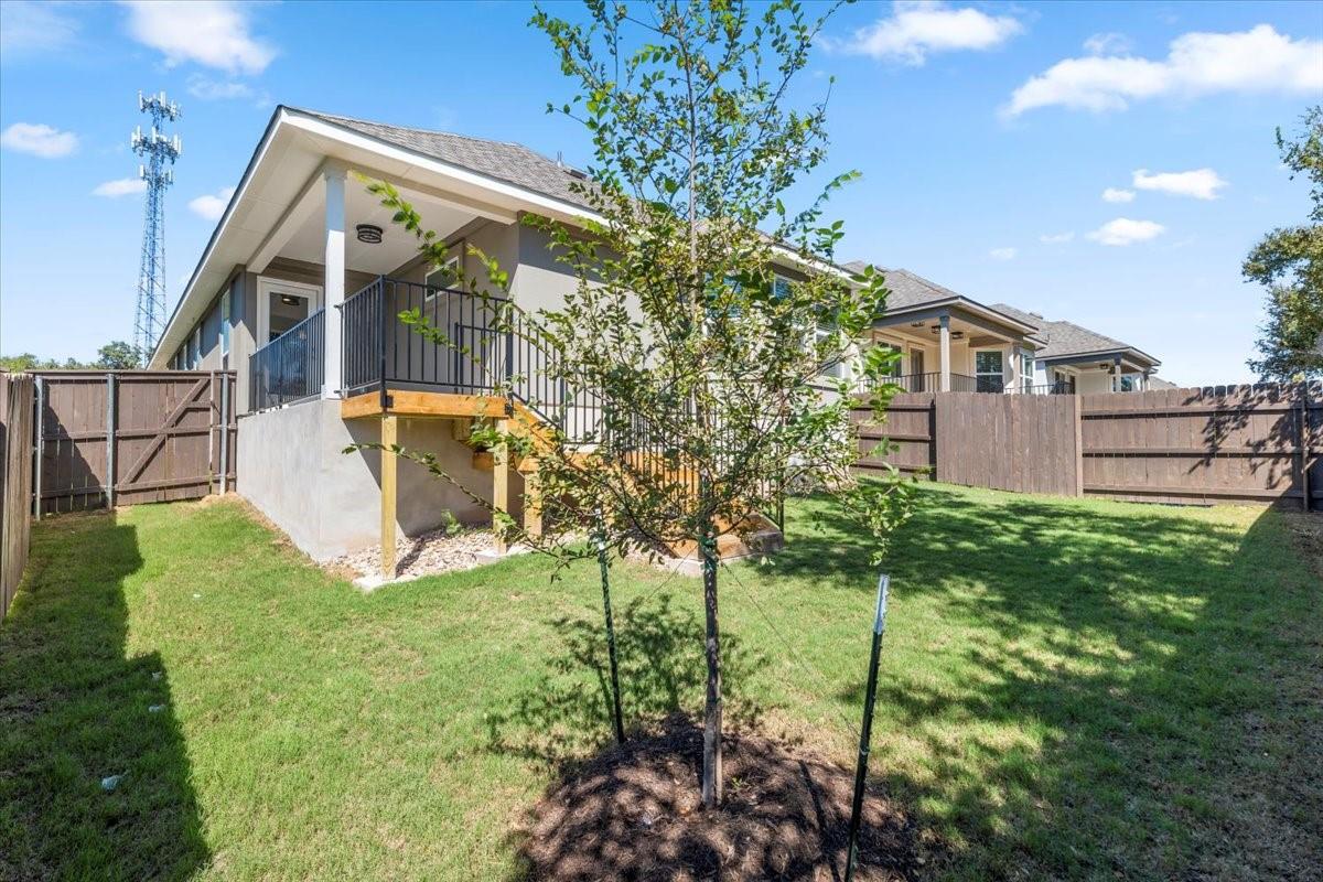 Home’s rear deck overlooks a fenced grassy yard with a young tree.
