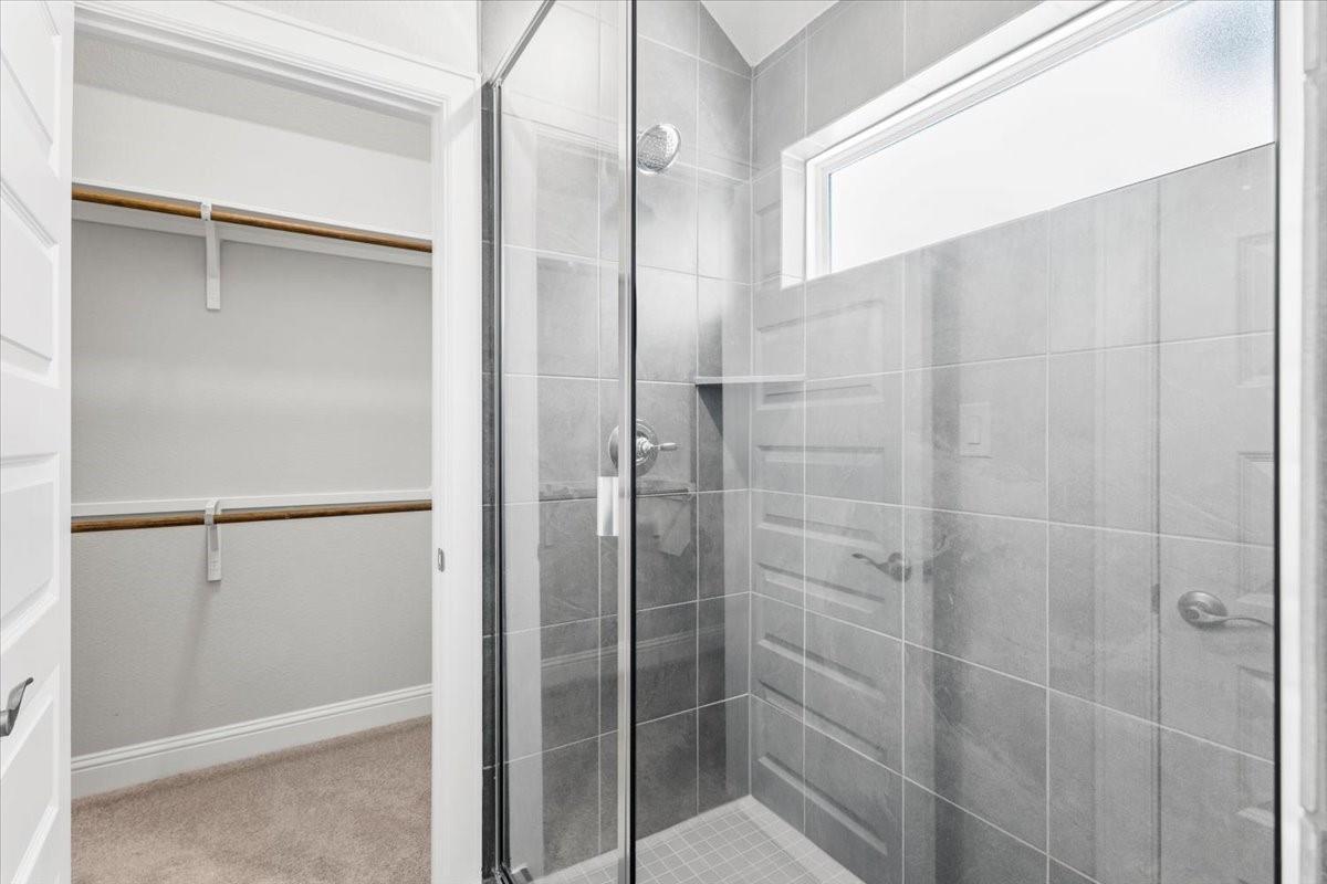 Bathroom with a glass-enclosed gray-tiled shower beside an open closet.