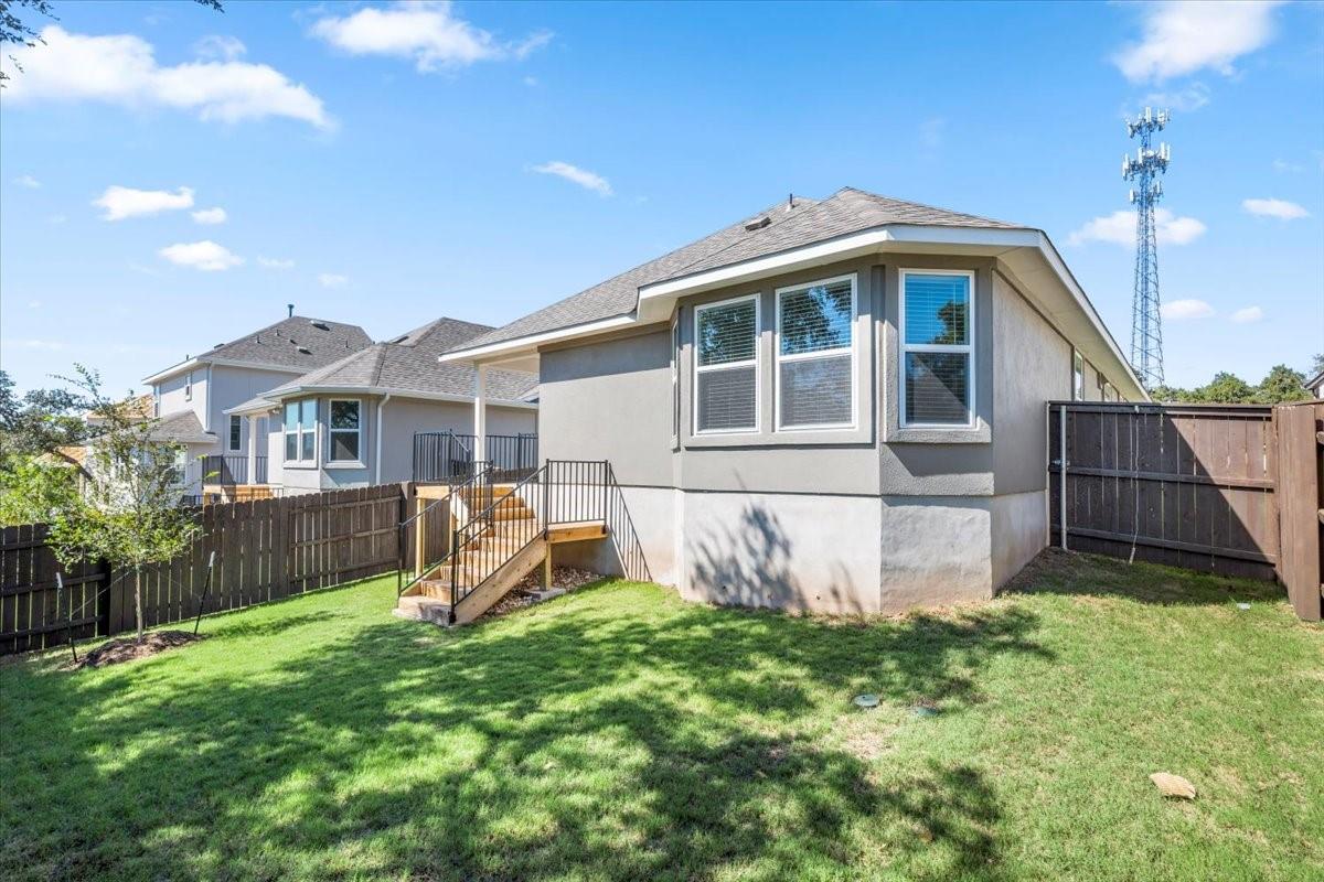 Gray stucco home with a raised wooden deck and steps overlooking a fenced grassy backyard.
