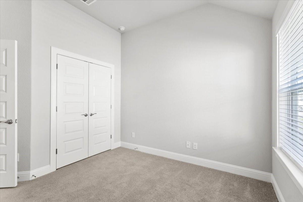 Empty bedroom with beige carpet, double closet doors, and a large window with blinds.
