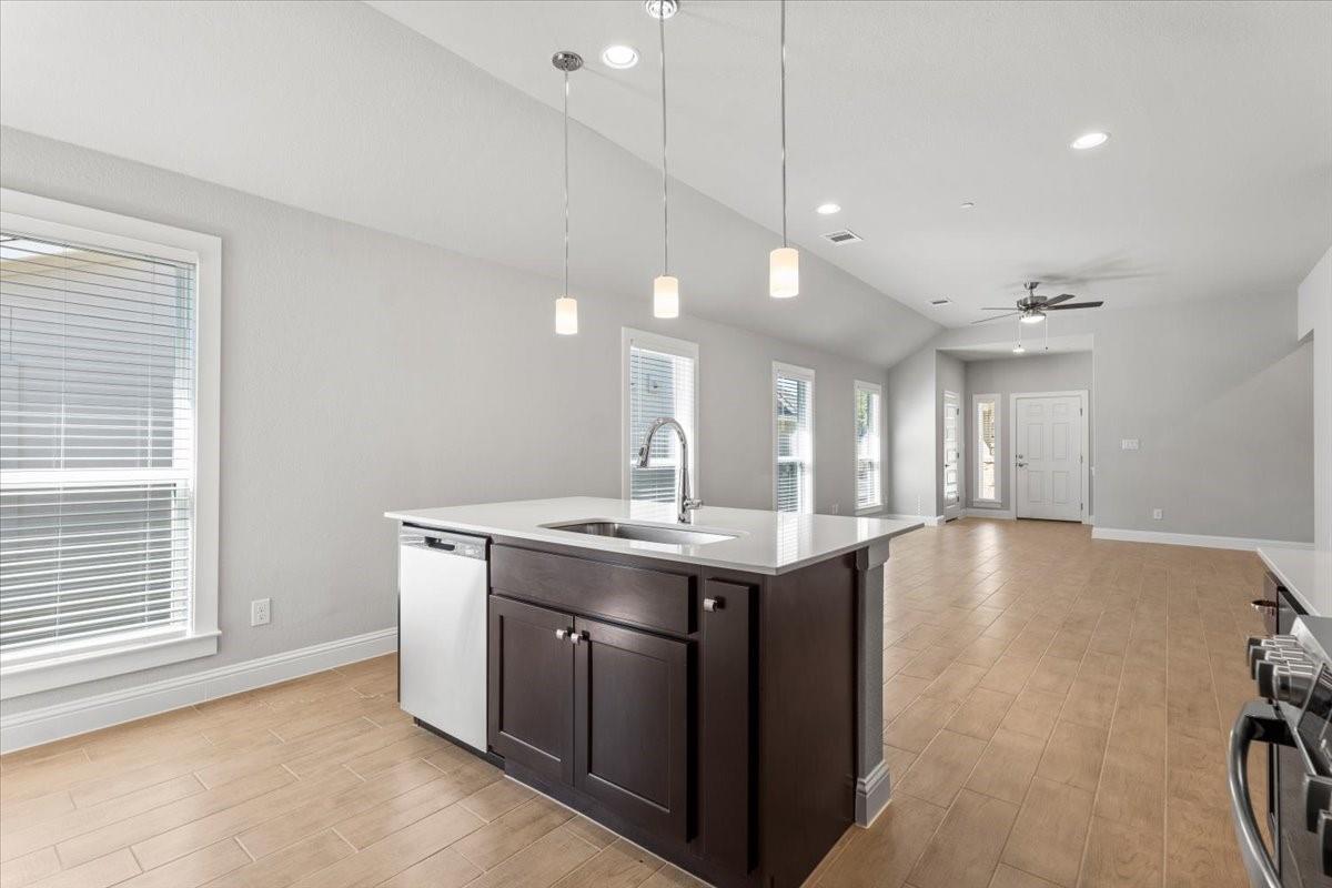 Open-plan kitchen with a dark island, white countertop, pendant lights, and tan tile flooring.