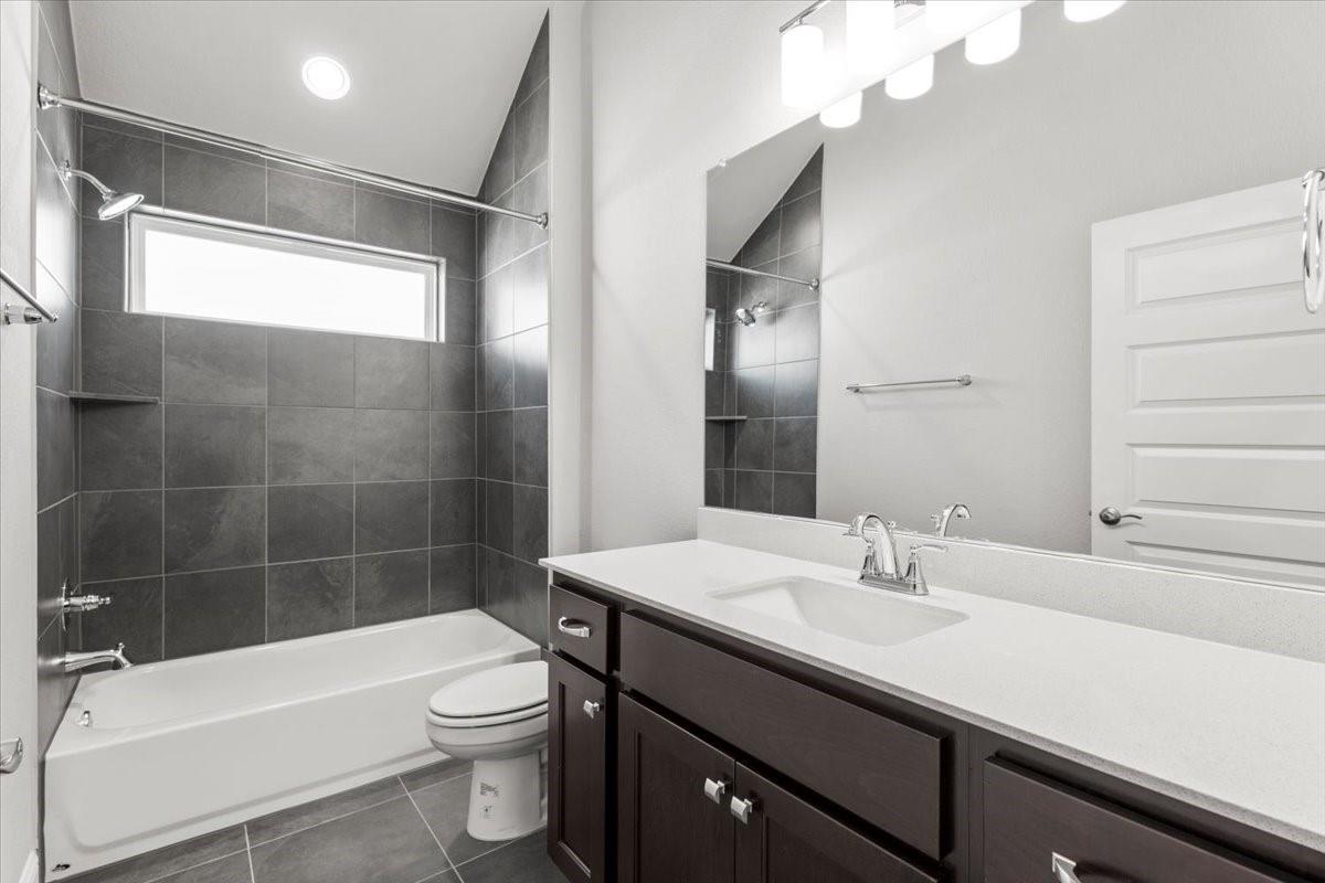 Bathroom with a dark gray tiled tub and shower beside a dark wood vanity and wide mirror.