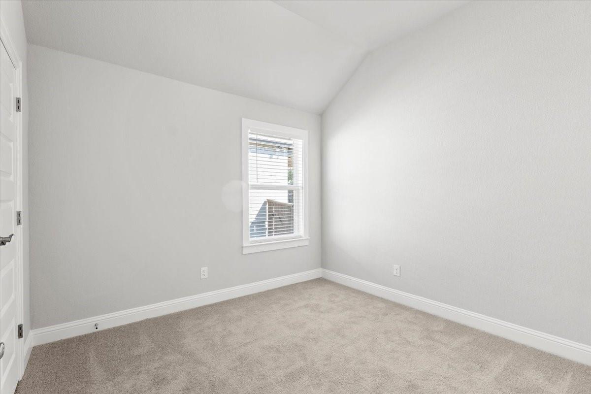 Empty bedroom with a vaulted ceiling, light carpet, and a window with white blinds.