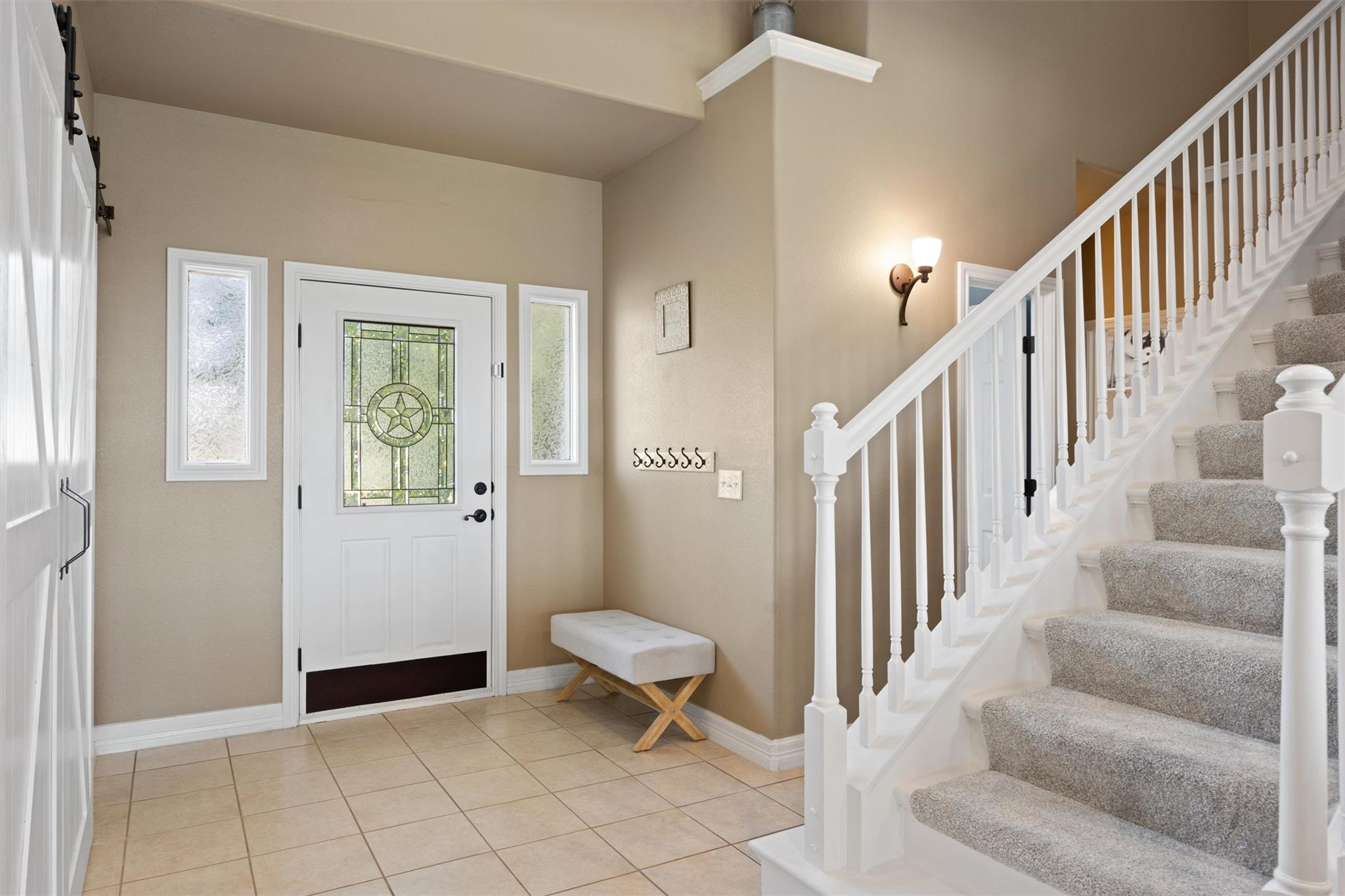 Entry foyer with a decorative glass front door, tiled floor, bench, and carpeted staircase.