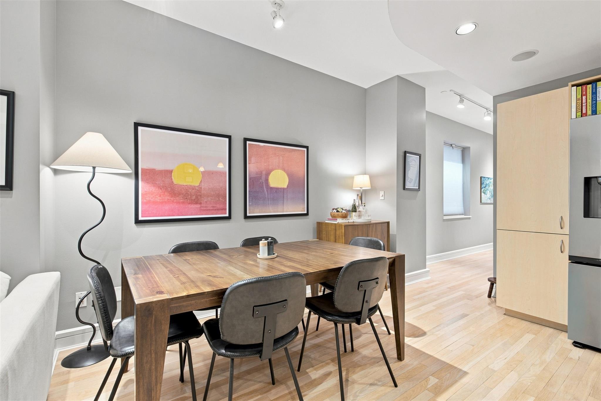 Furnished condo dining area with a wooden table, gray chairs, colorful wall art, and pale wood flooring.