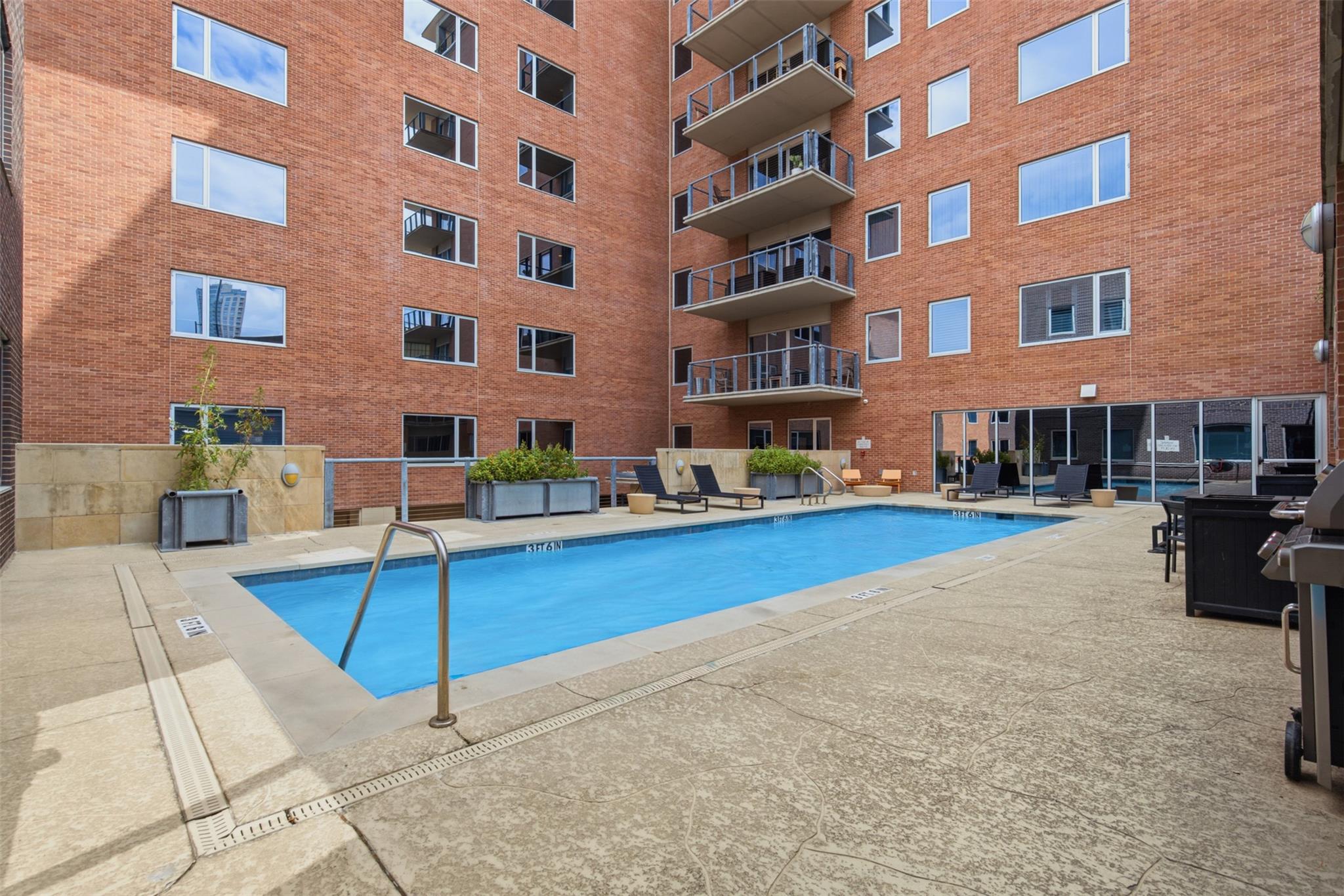 Courtyard swimming pool surrounded by brick apartment buildings, balconies, and lounge chairs.