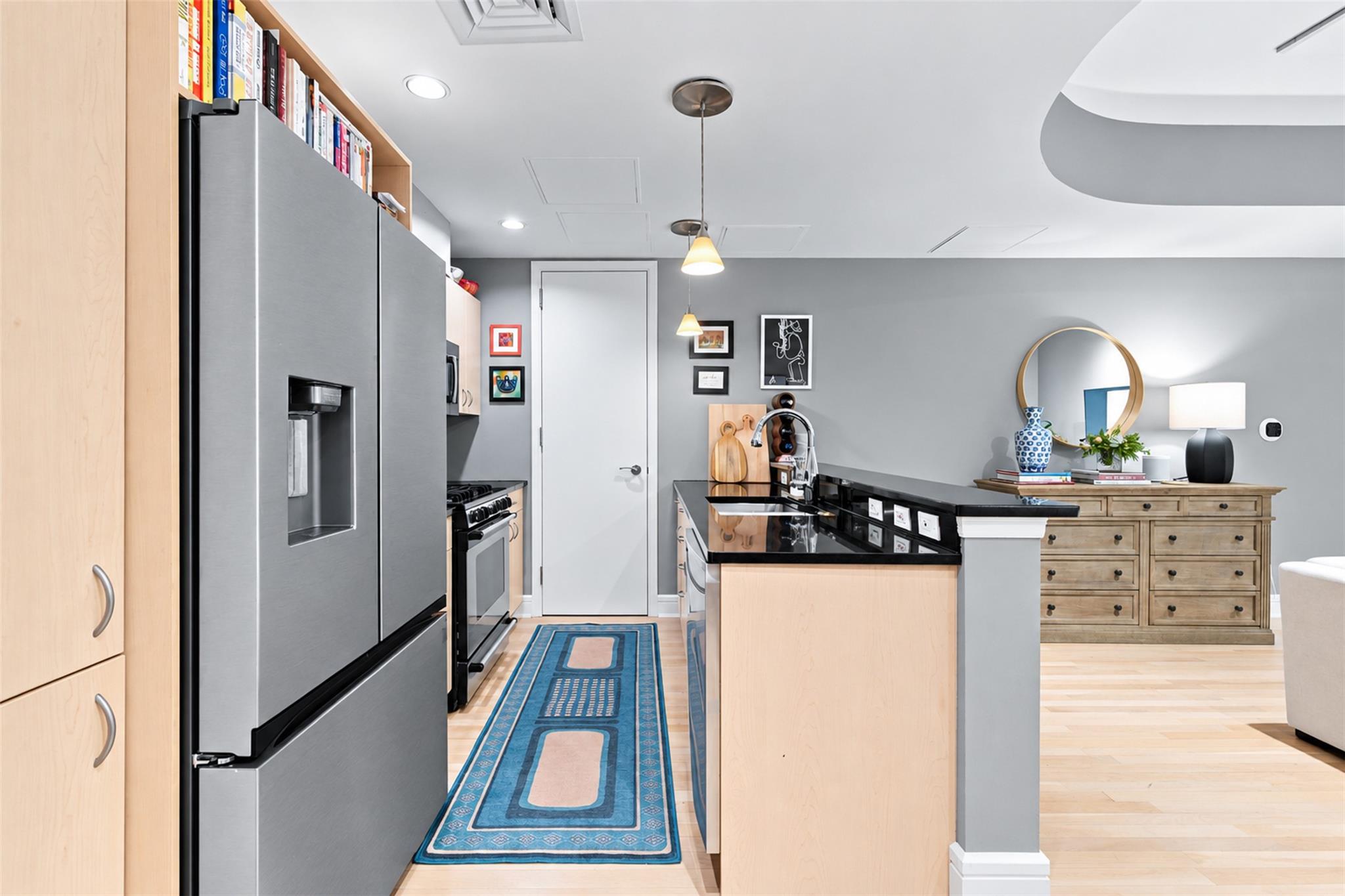 Kitchen with light wood cabinetry, stainless steel appliances, black counters, and a large island.