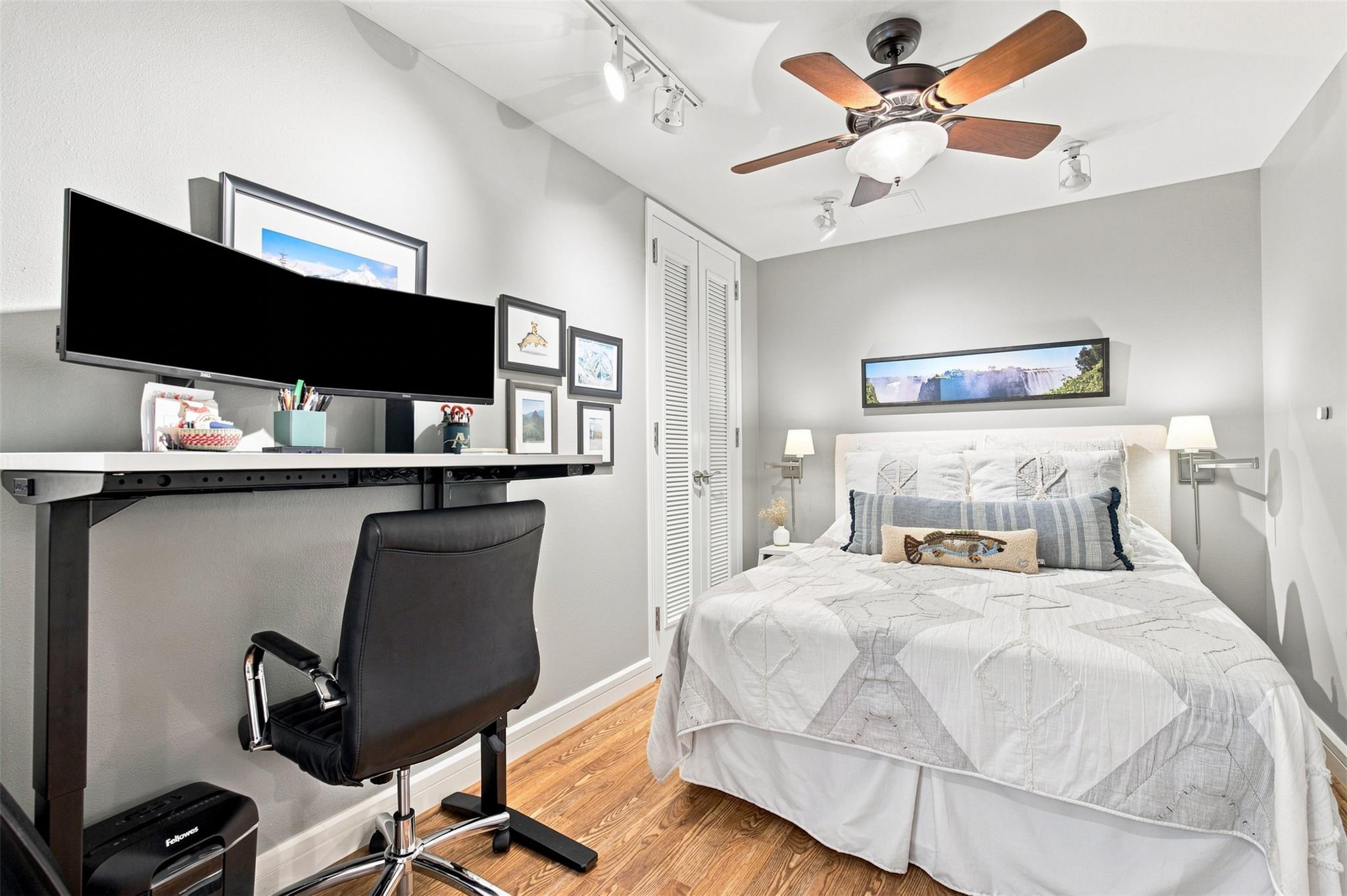 Bedroom with a white quilted bed and a desk workstation with a large monitor.