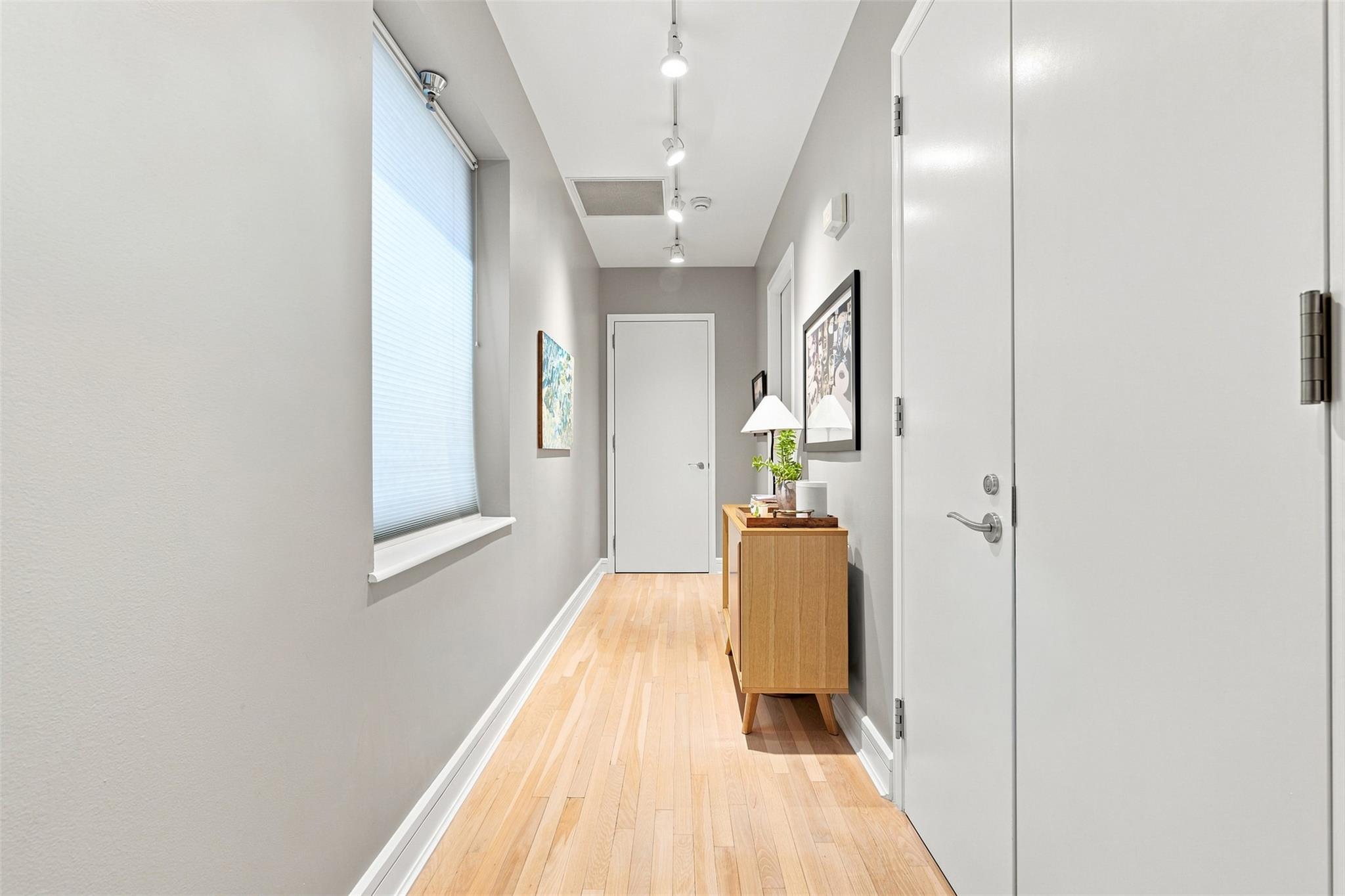 Condo entry hallway with pale hardwood floors, a shaded window, and a wood console table.