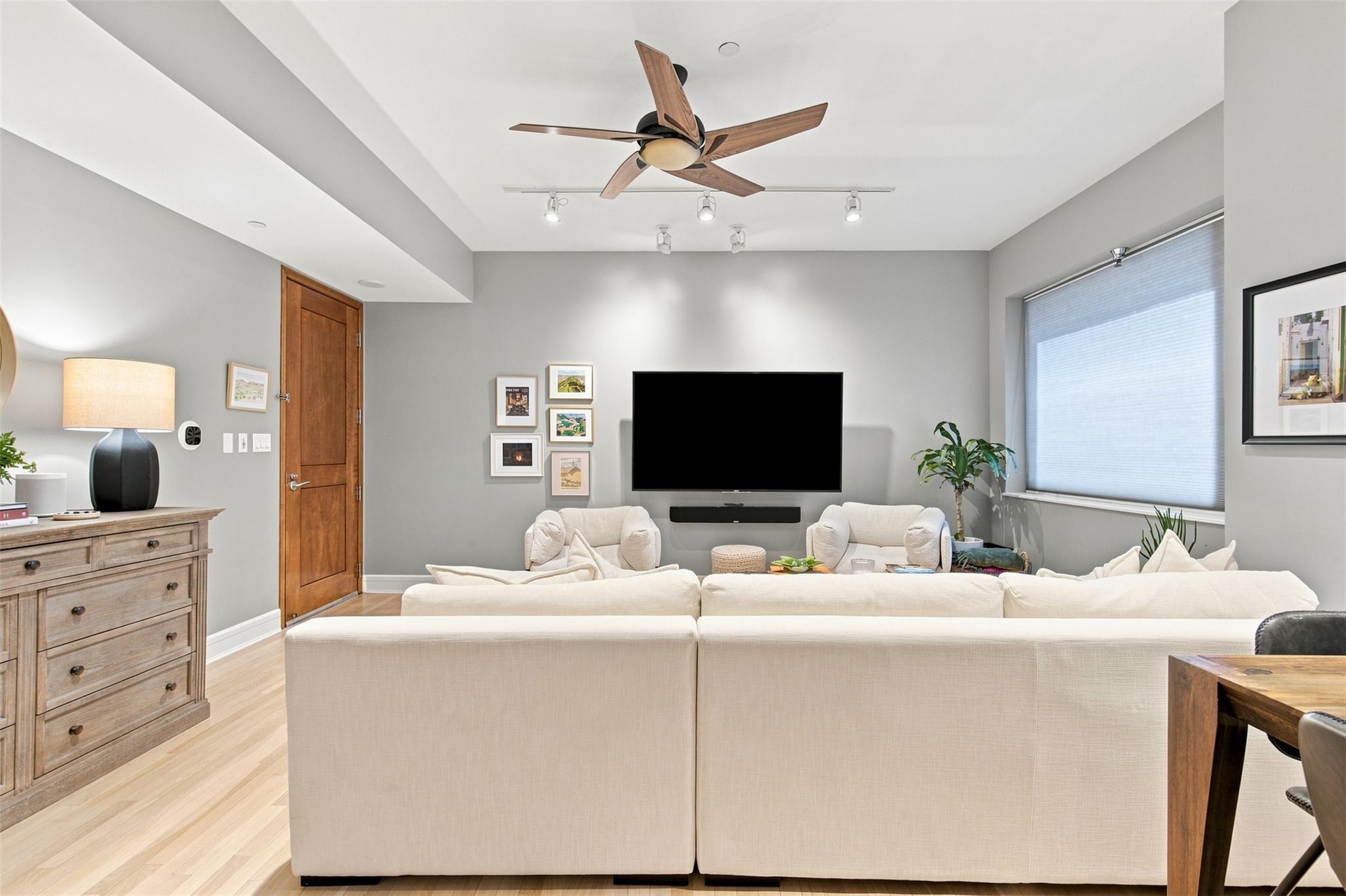 Living room with a large cream sectional sofa, wall-mounted television, and wood-blade ceiling fan.