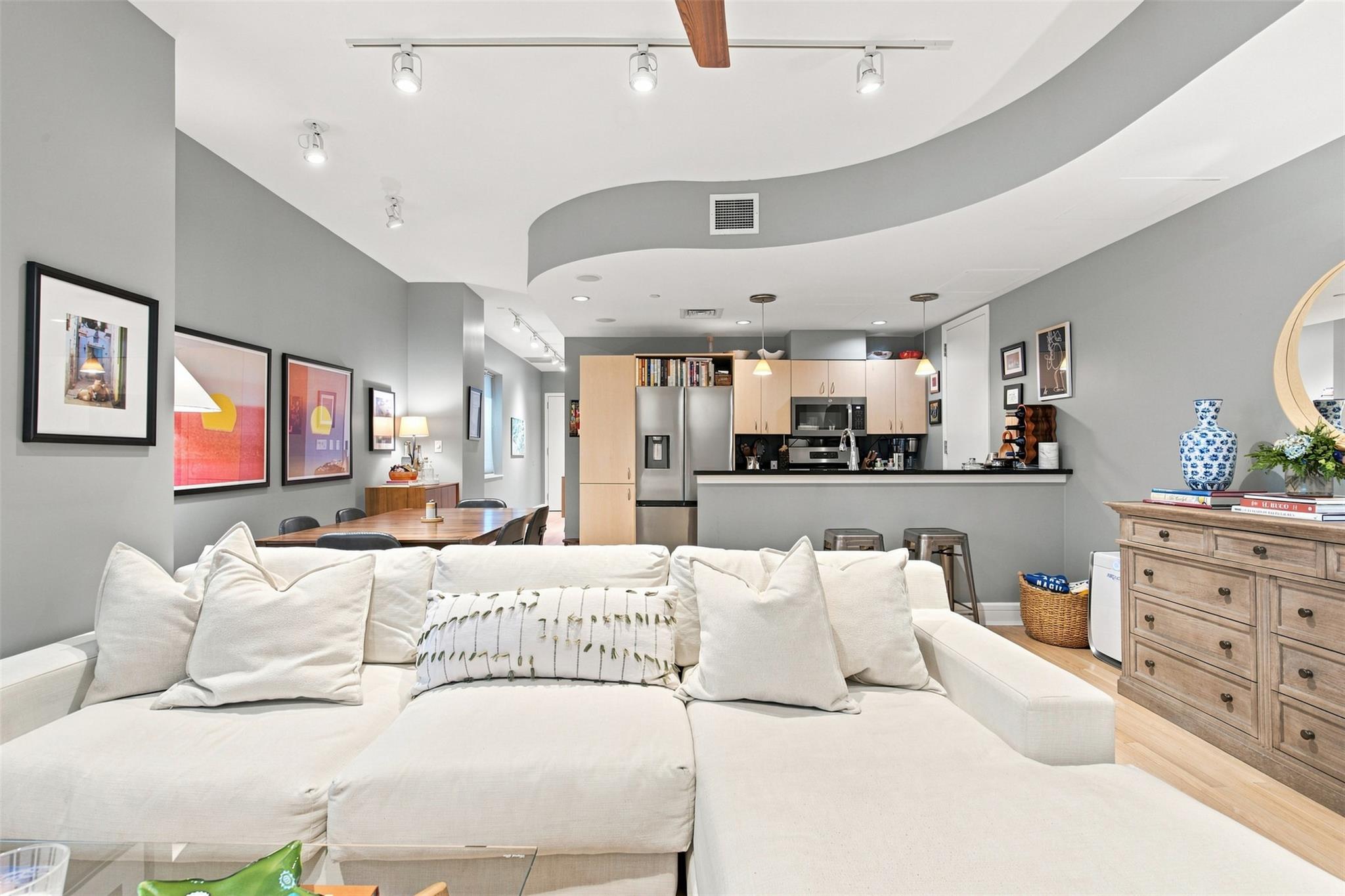 Open-plan condo living room with a white sectional facing the dining area and kitchen.