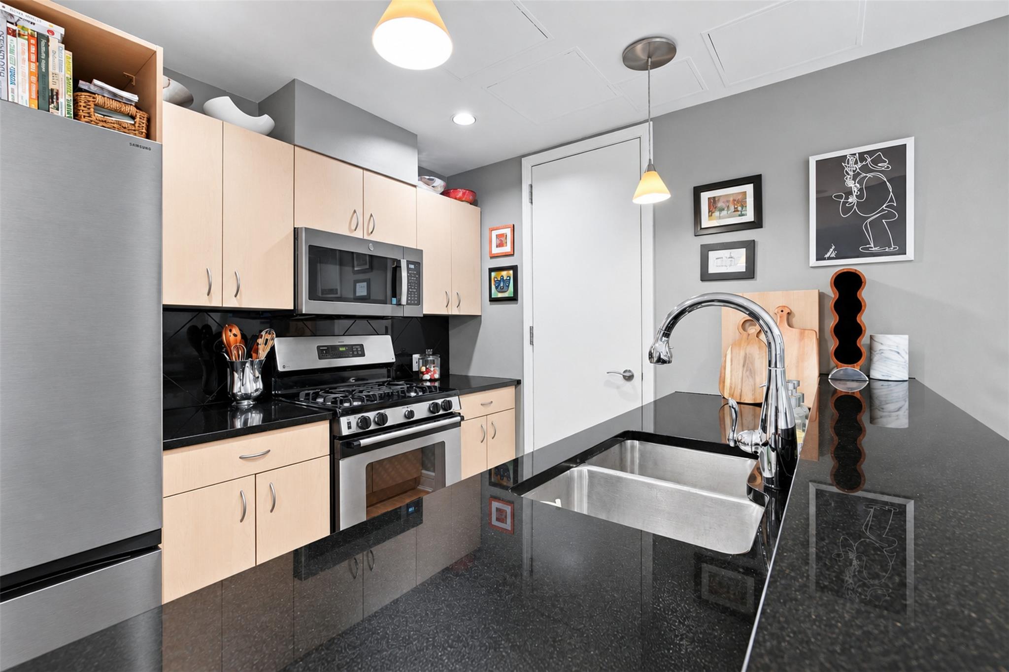 Modern kitchen with pale wood cabinets, stainless steel appliances, and a black island with a double-basin sink.