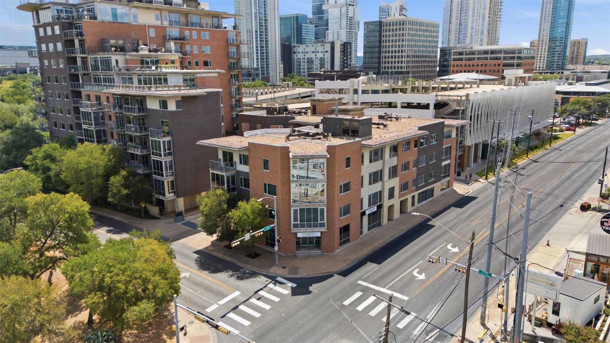 Downtown condominium building with glass balconies at a tree-lined Austin intersection, surrounded by high-rises.