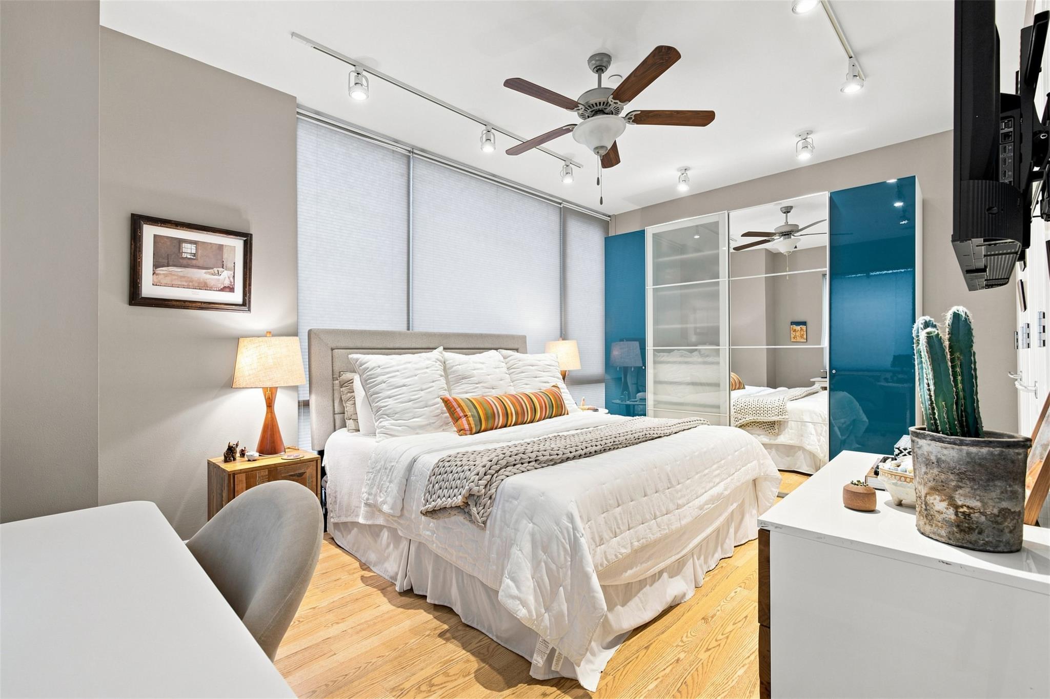 Bedroom with a white bed, mirrored wardrobe with blue panels, and light wood floors.