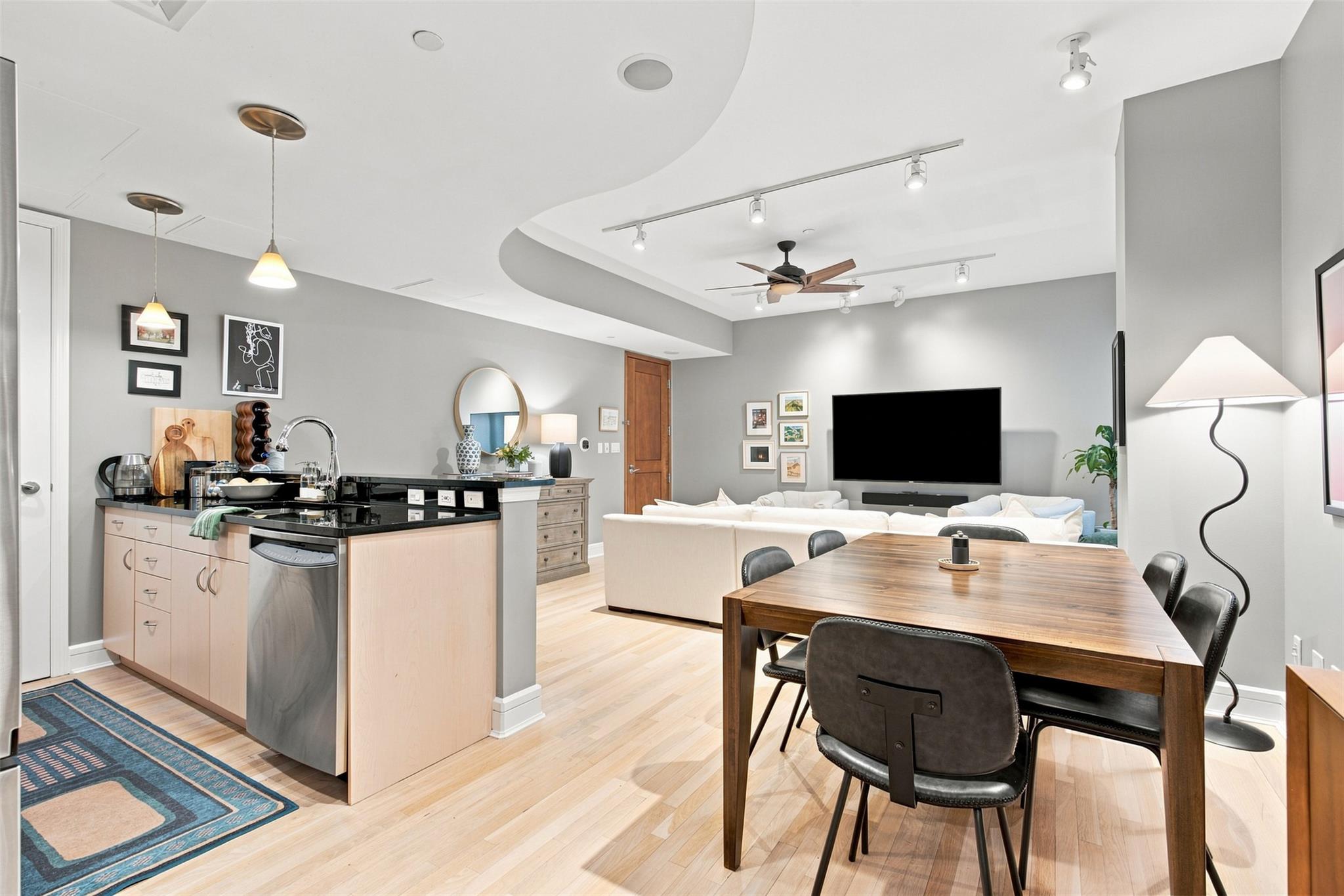 Open-plan condo kitchen, dining, and living area with a black-countertop island and light wood floors.