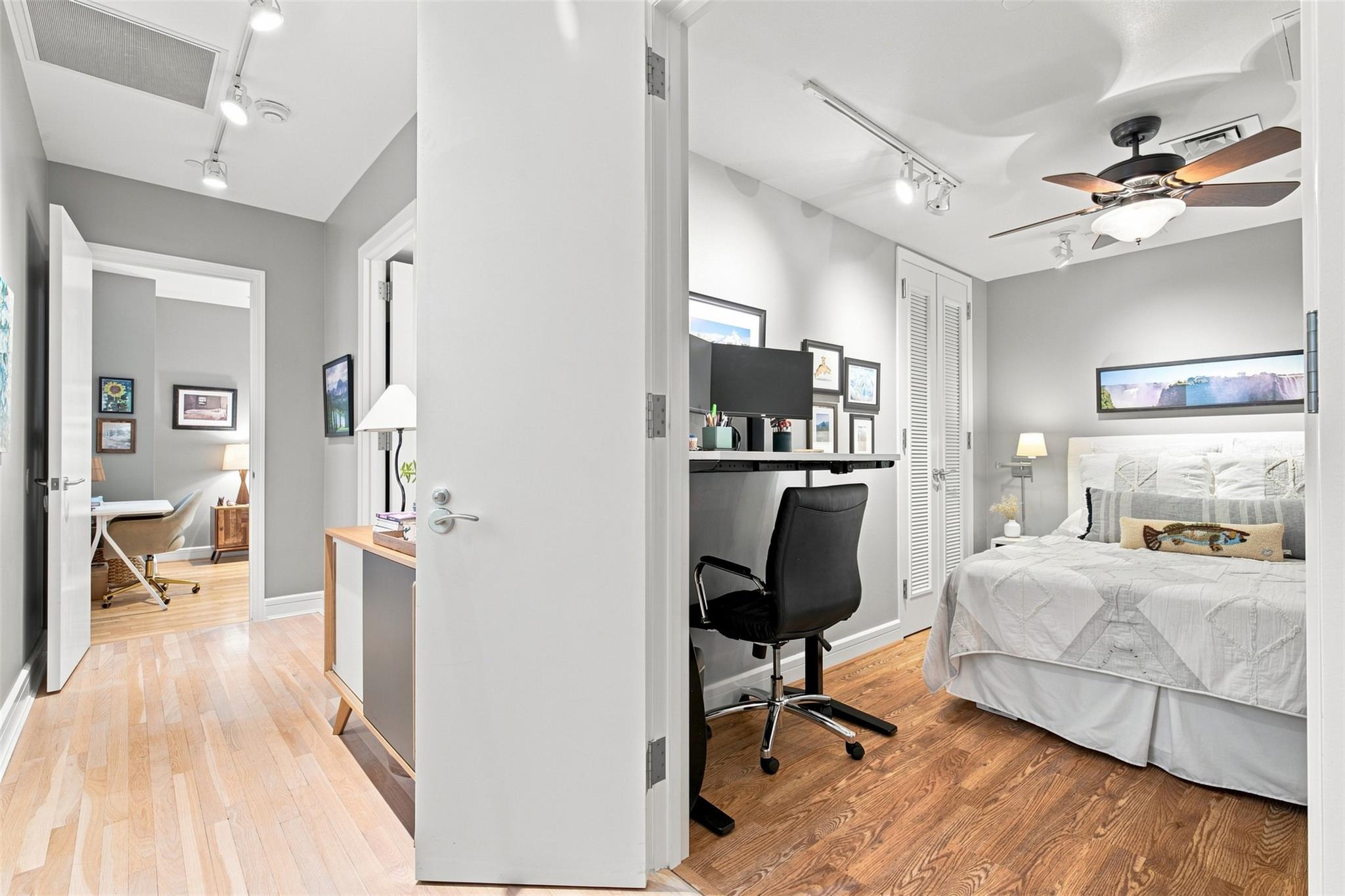 Bedroom with a white bed, wood floors, ceiling fan, and built-in desk with black chair.