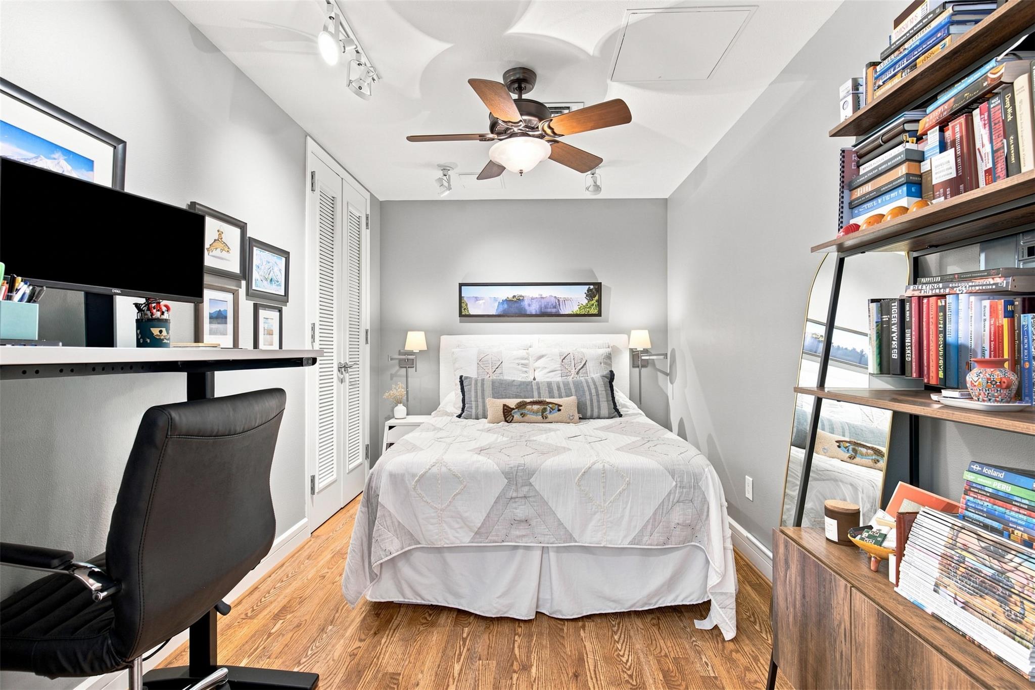 Furnished bedroom with a white bed, hardwood floors, desk, and book-filled shelving.