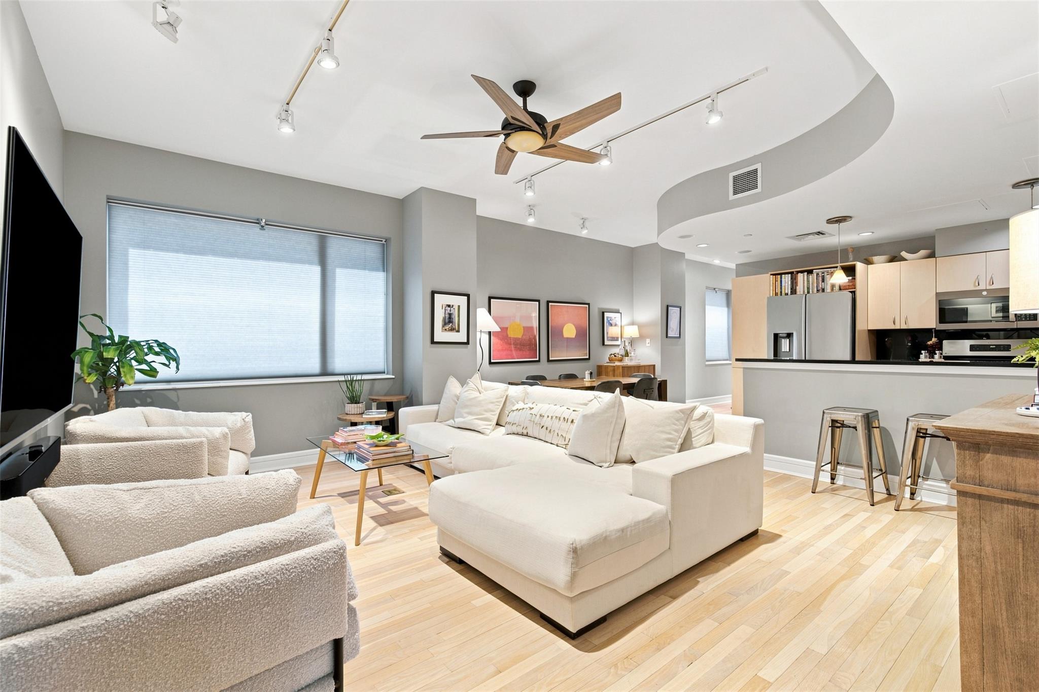 Open-plan condo living room with white sectional seating, light wood floors, and an adjoining kitchen.