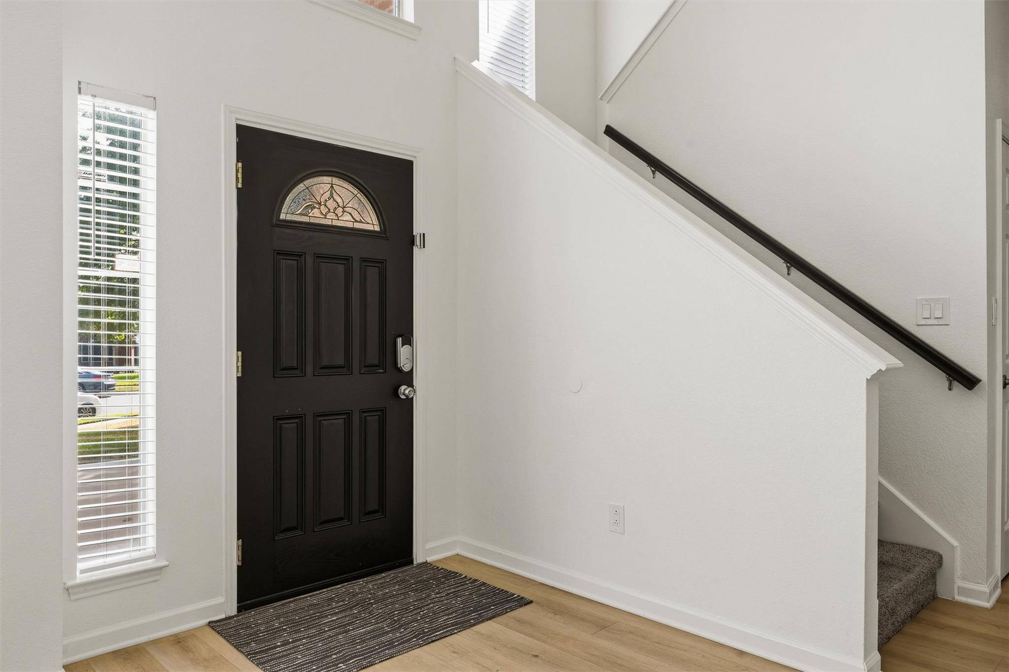 Entry foyer with a dark front door, arched glass insert, tall window, and staircase.