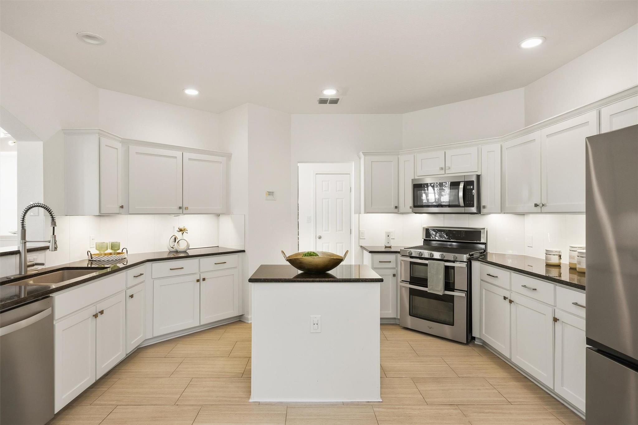 Kitchen with white shaker cabinets, stainless steel appliances, dark counters, and a central island.