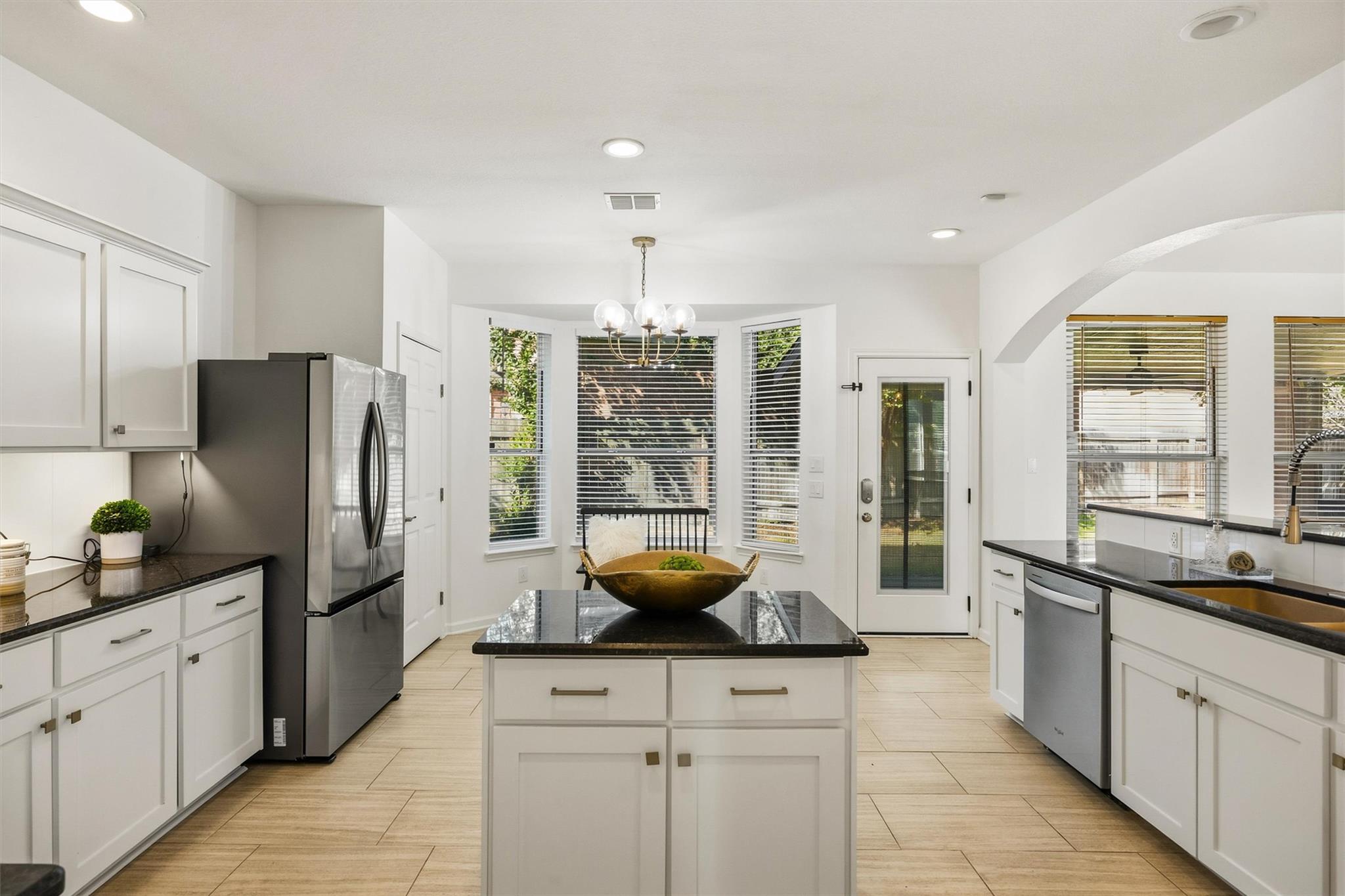 Bright white kitchen with a black granite island, stainless steel appliances, and a bay window.