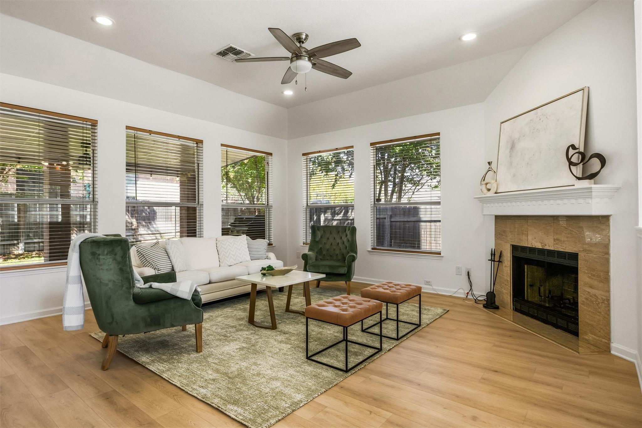 Living room with a stone fireplace, large windows, white sofa, and green armchairs.