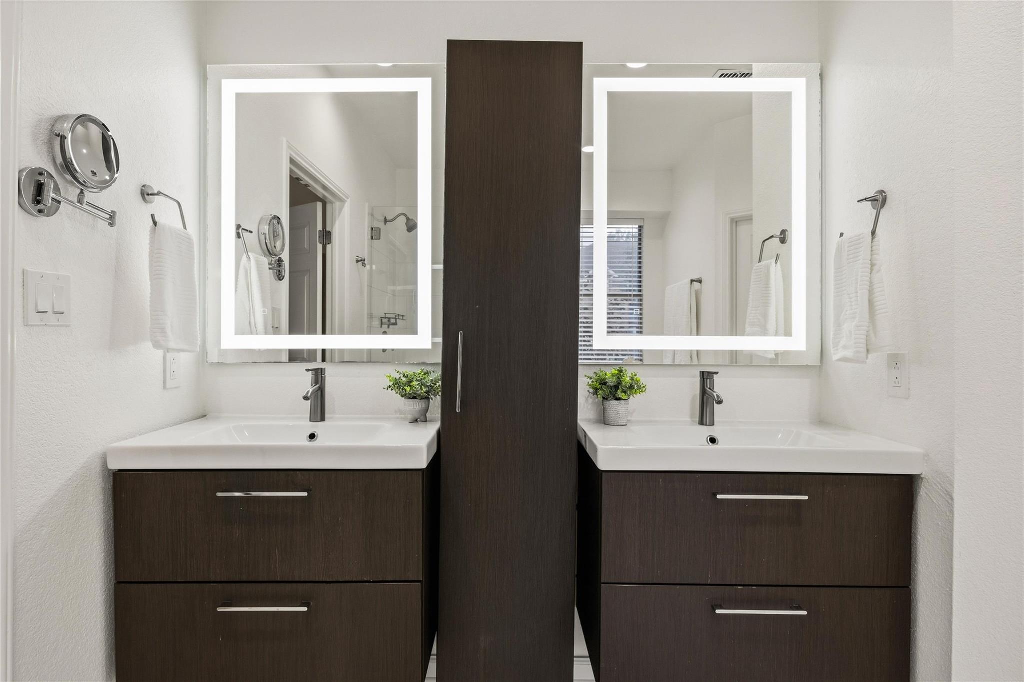 Bathroom with double sinks, dark wood vanities, and illuminated rectangular mirrors.