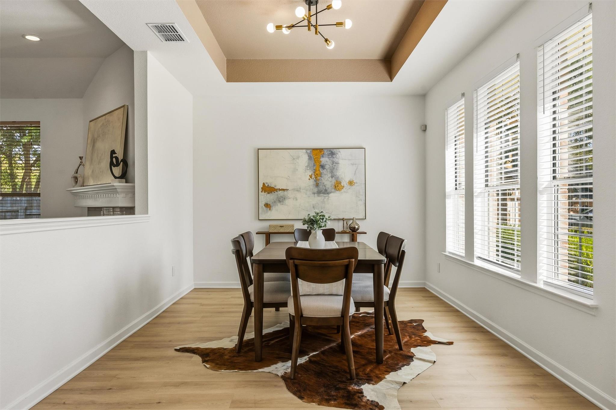 Dining room with a dark wood table, hide rug, abstract artwork, and tall windows with white blinds.