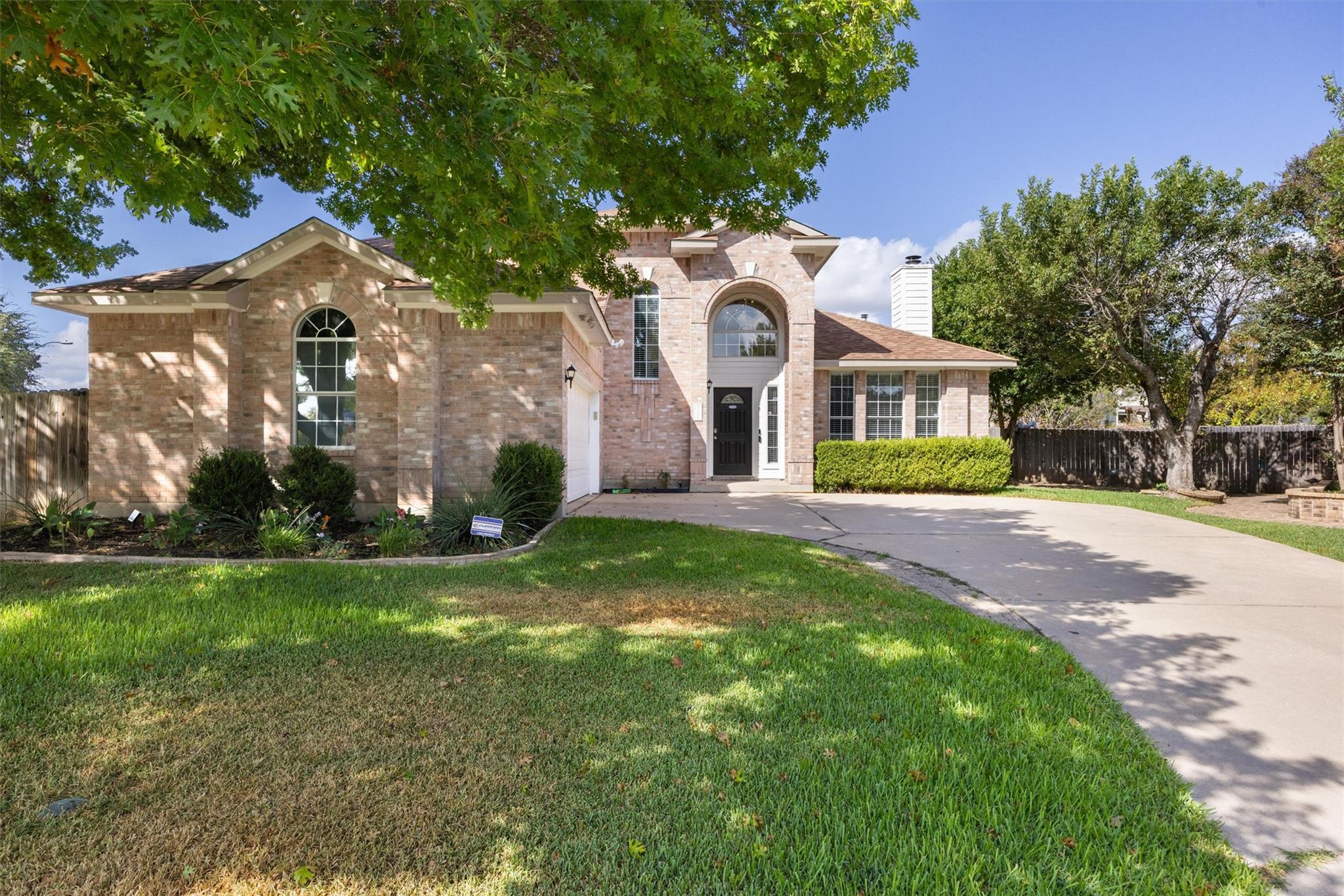 Two-story brick house with arched windows, a curved driveway, and a tree-shaded lawn.