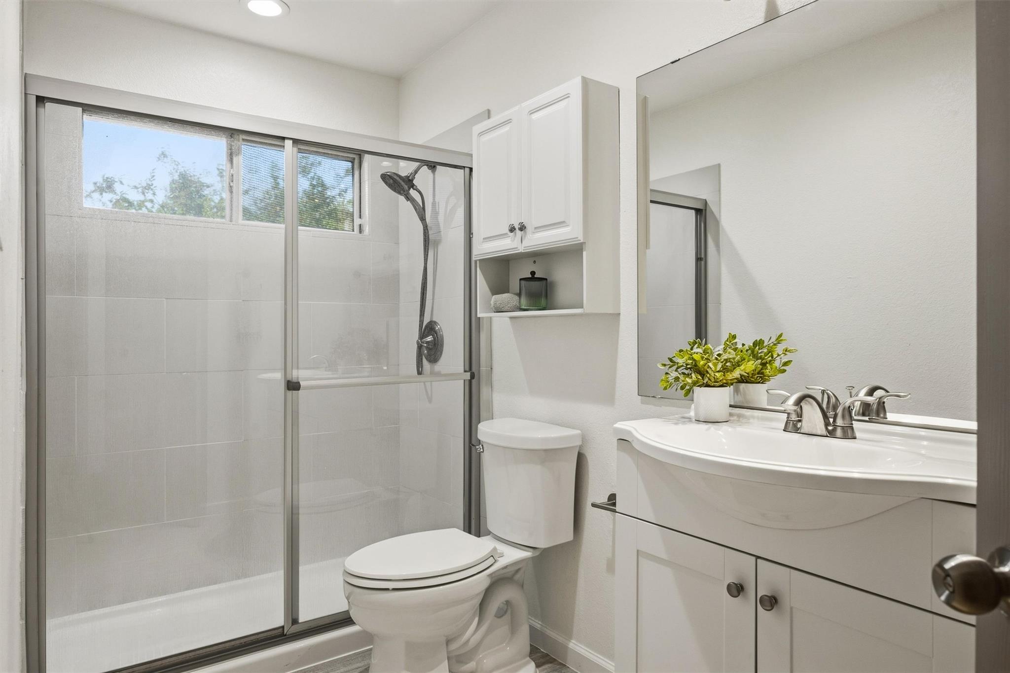 Bathroom with a tiled tub-shower enclosure, high windows, and a white vanity with a large mirror.