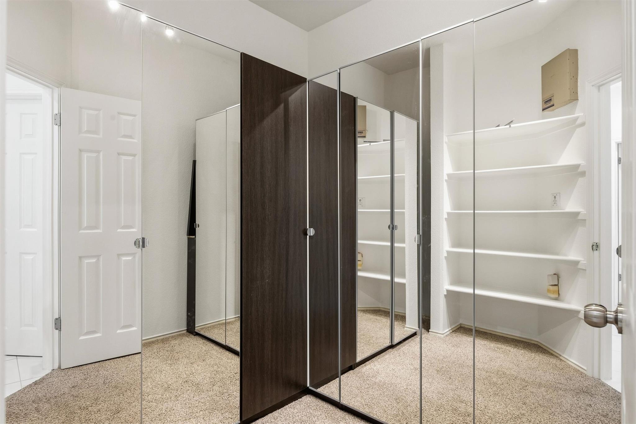 Walk-in closet with mirrored wardrobe doors and built-in white shelving.