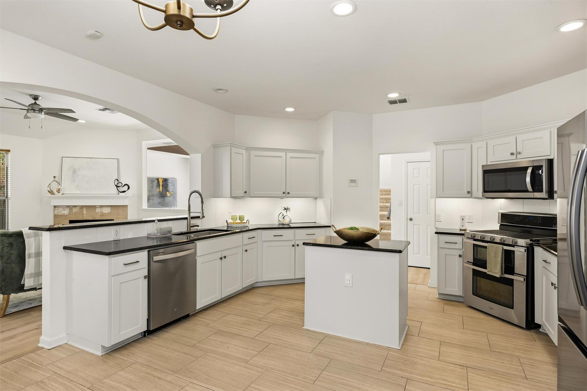 Open kitchen with white cabinets, black countertops, a large island, and stainless steel appliances.