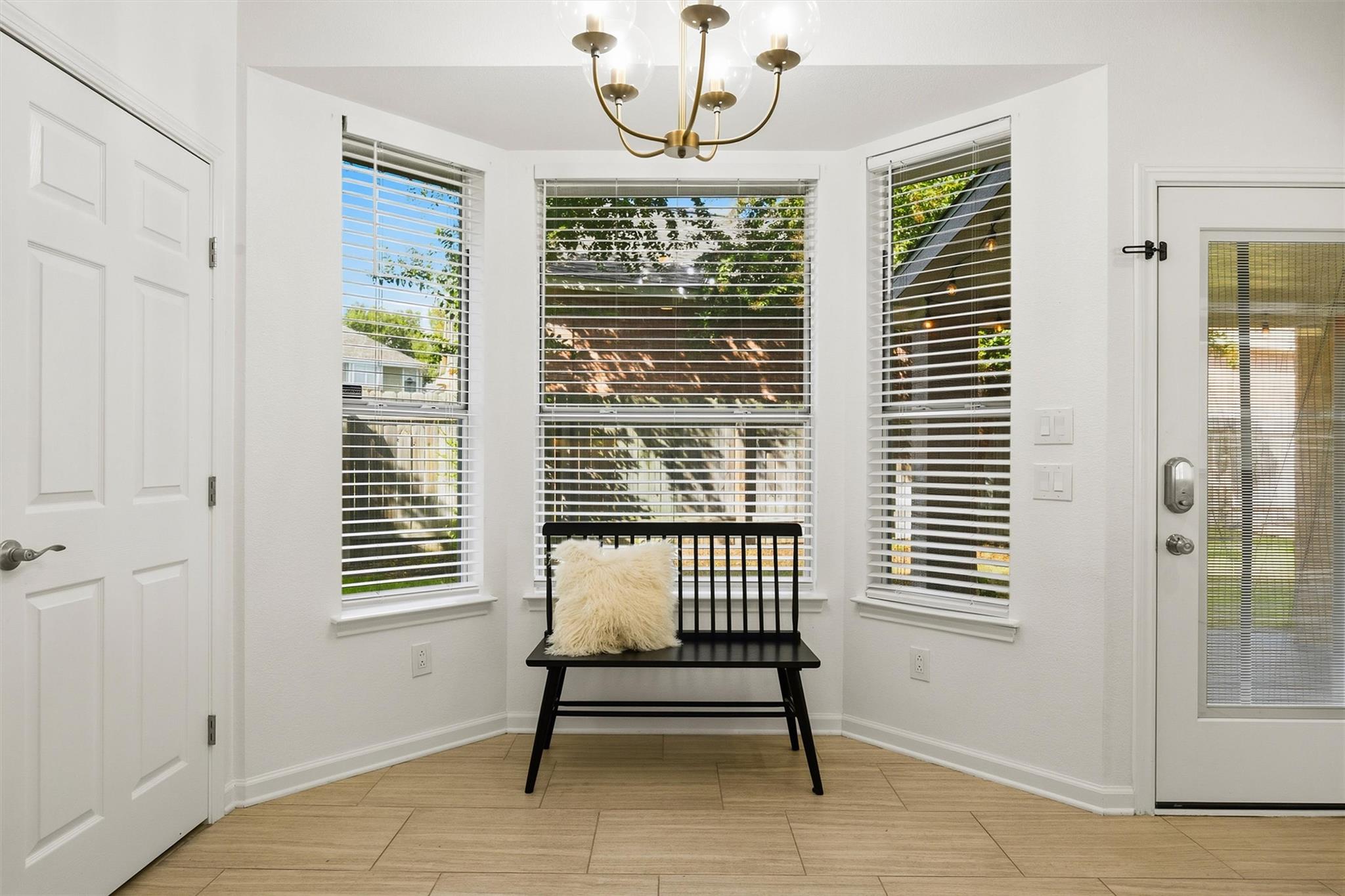 Front entry with a black bench beneath three windows with white blinds and a brass chandelier.