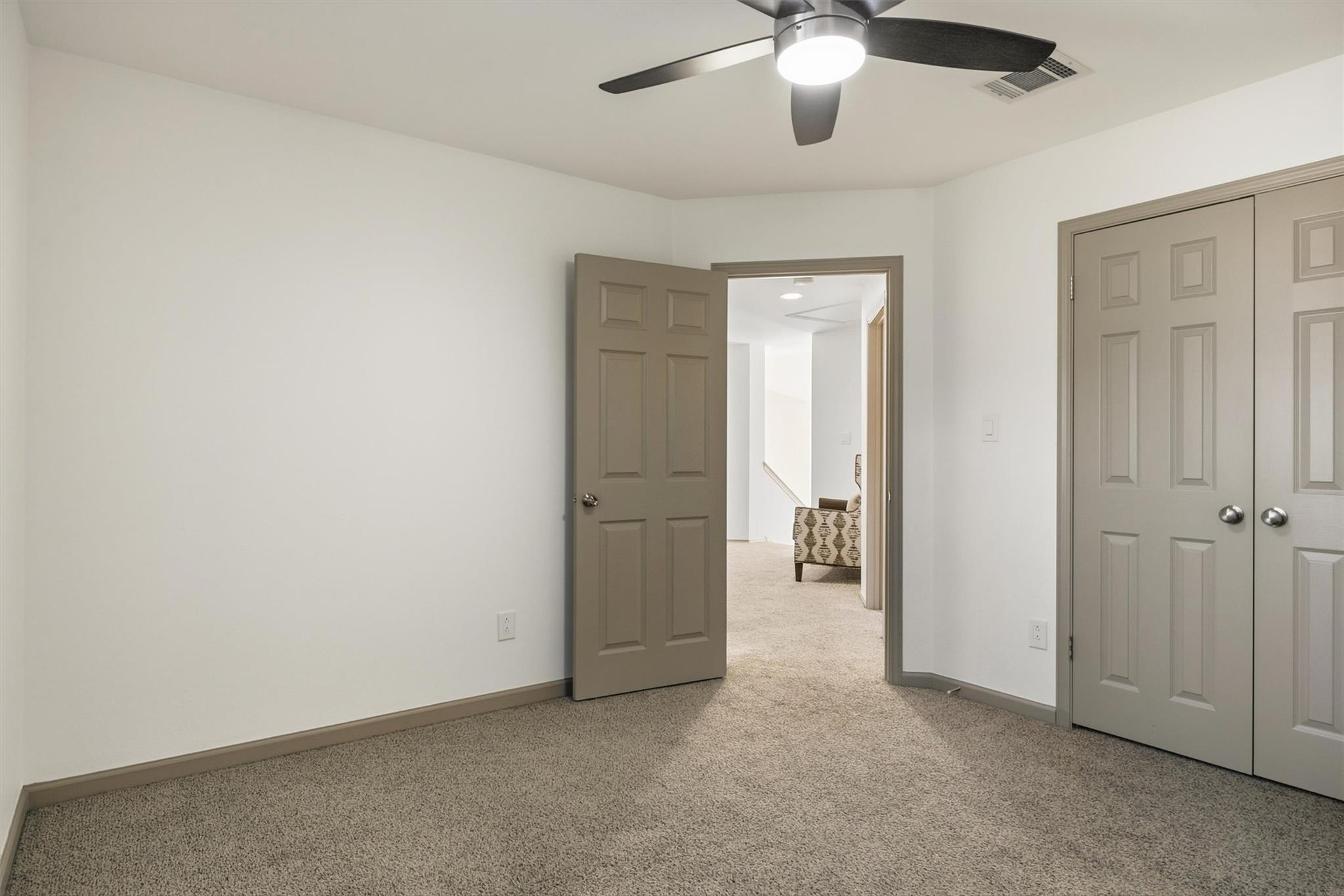 Empty carpeted bedroom with a ceiling fan, double closet doors, and an open doorway.