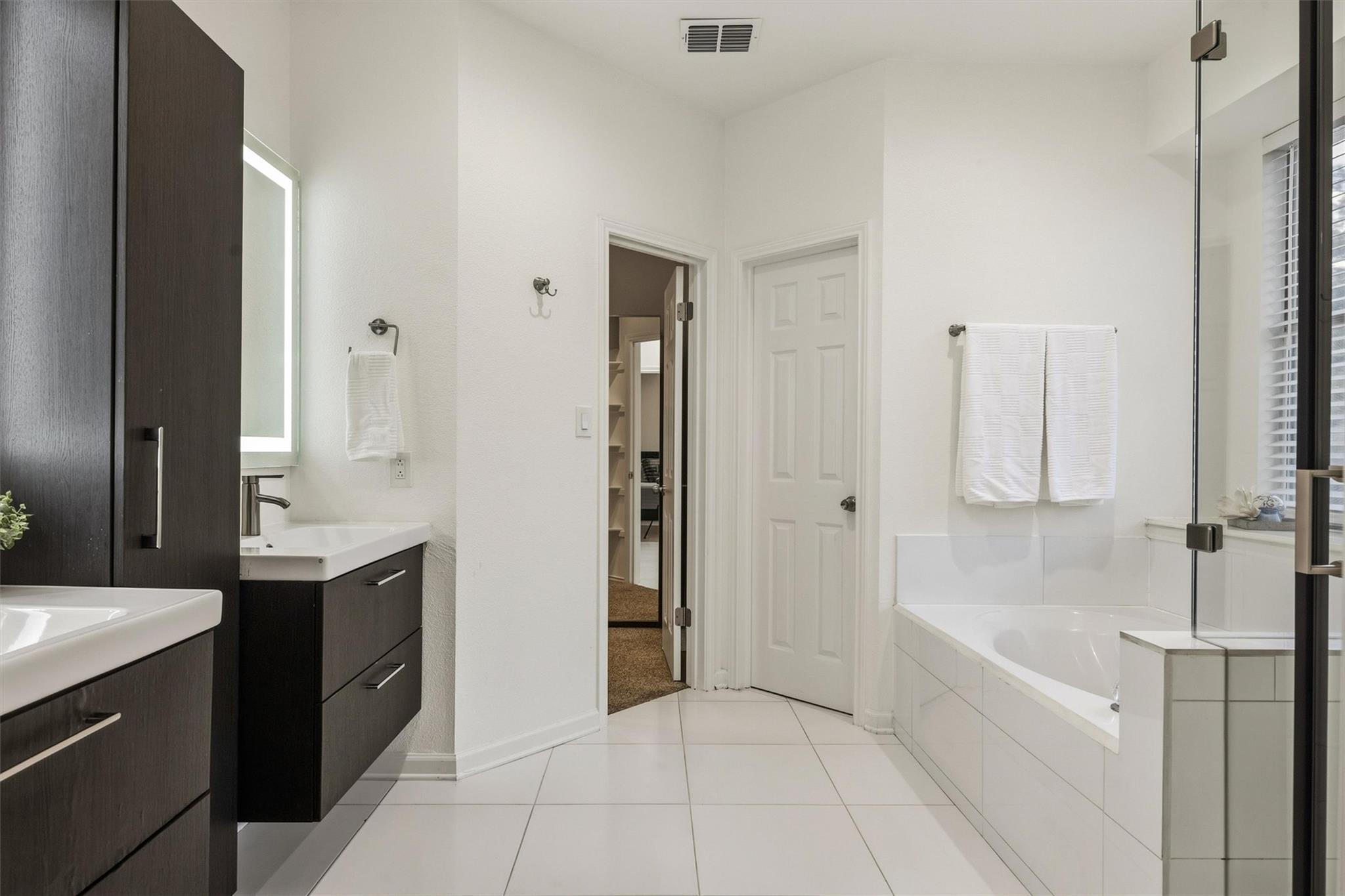 Bathroom with a dark wood vanity, white tile, and a bathtub behind a glass shower screen.