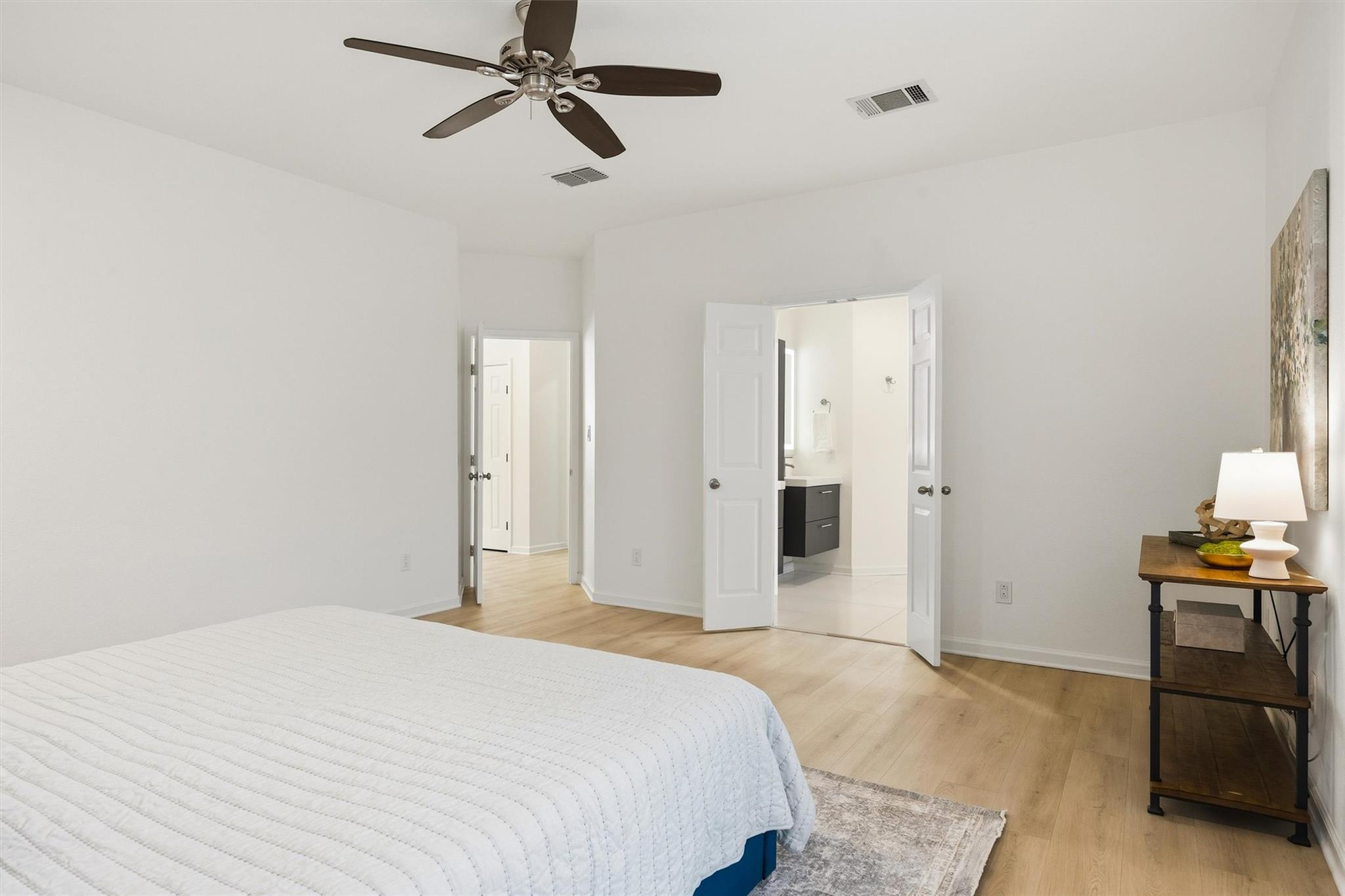 Bedroom with a white quilted bed, ceiling fan, and open doors to an en suite bathroom.