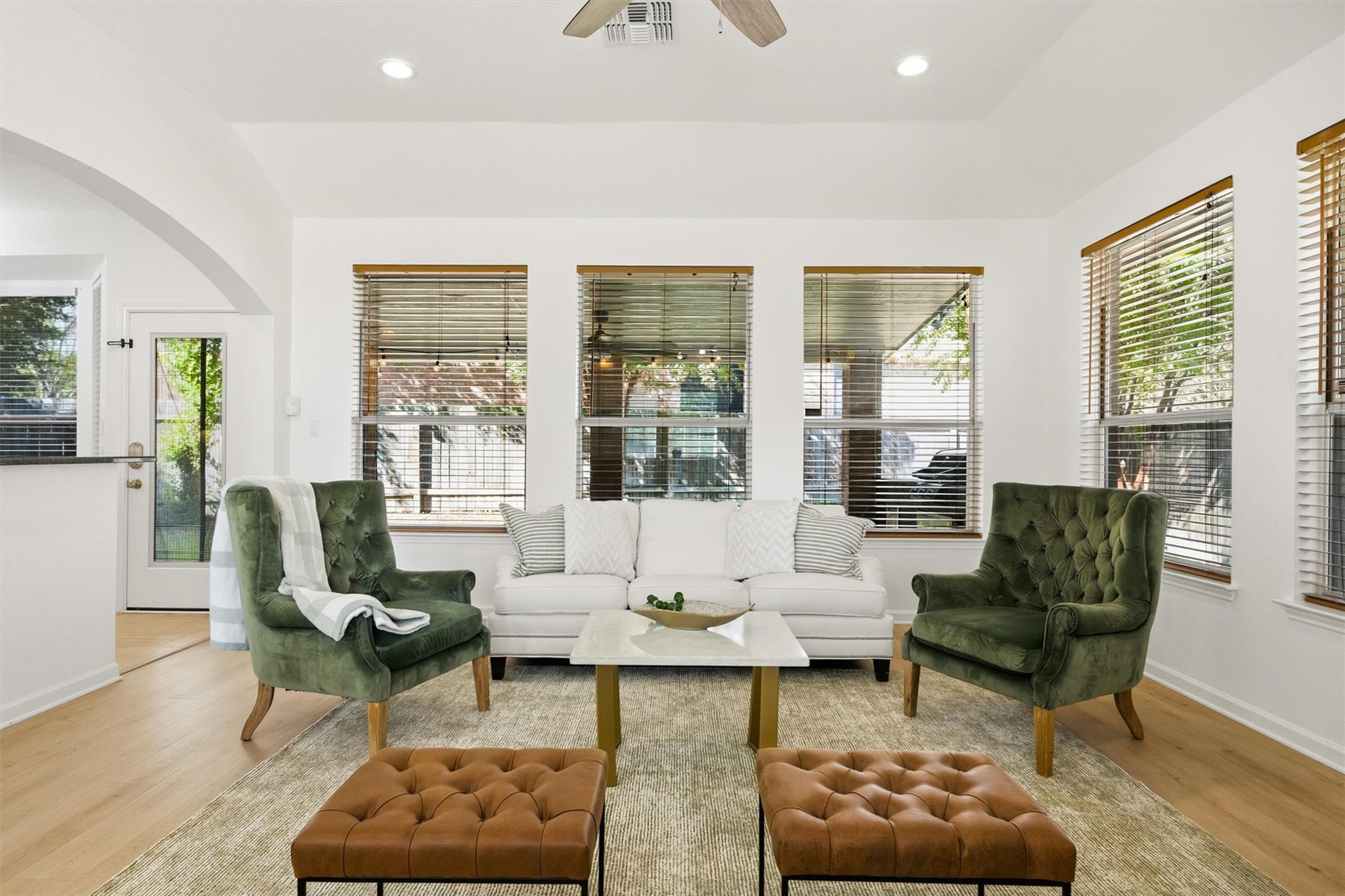 Living room with a white sofa, green armchairs, and large windows overlooking a covered patio.