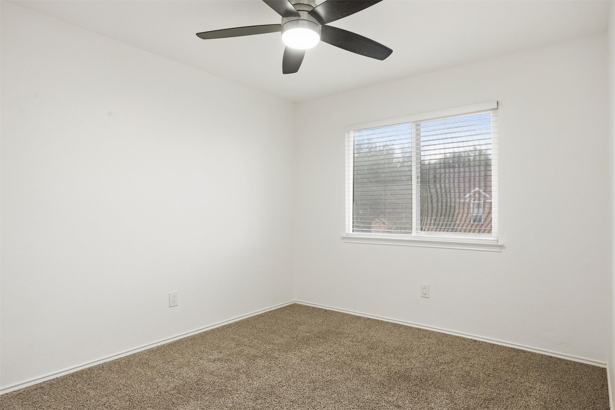 Vacant bedroom with beige carpet, a window with blinds, and a ceiling fan with light.