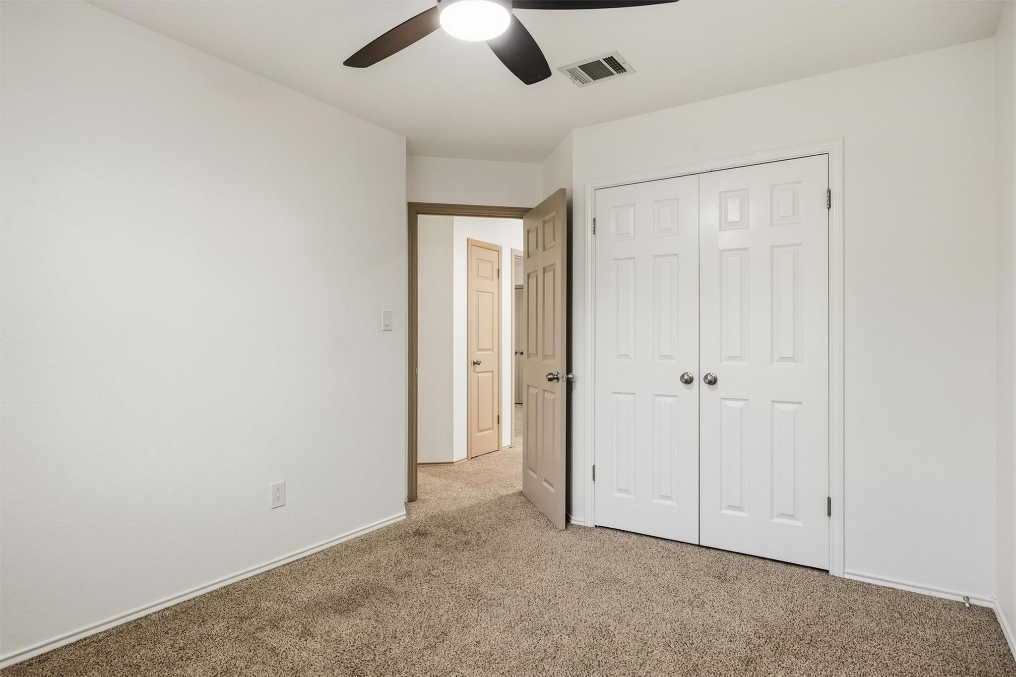 Empty carpeted bedroom with double closet doors and an open doorway to the hall.