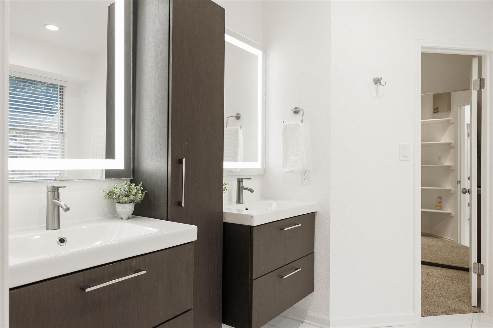 Modern bathroom with double sinks and dark wood vanities beside an open closet doorway.
