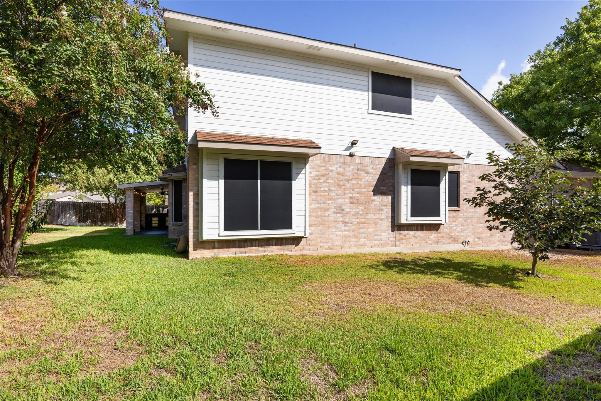 Rear of a two-story brick-and-siding house with large windows, a covered patio, and a grassy backyard.