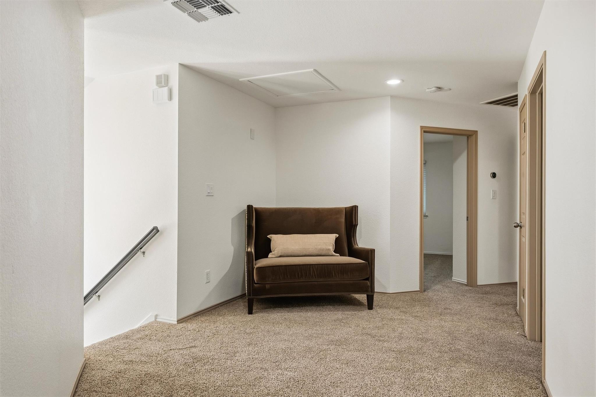 Carpeted landing with a brown chair, metal stair handrail, and several doorways.