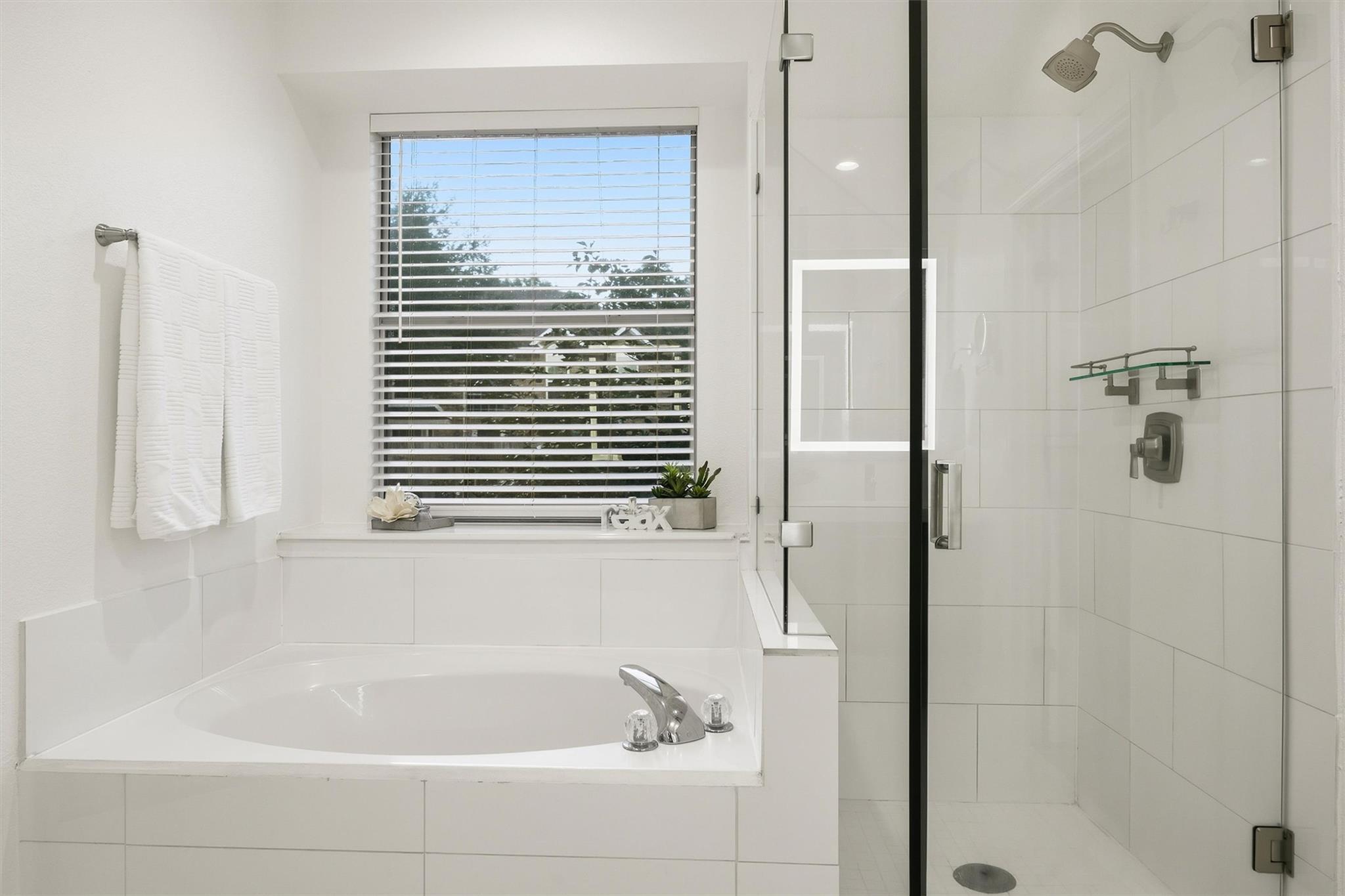 White bathroom with a soaking tub beneath a window and a glass-enclosed tiled shower.
