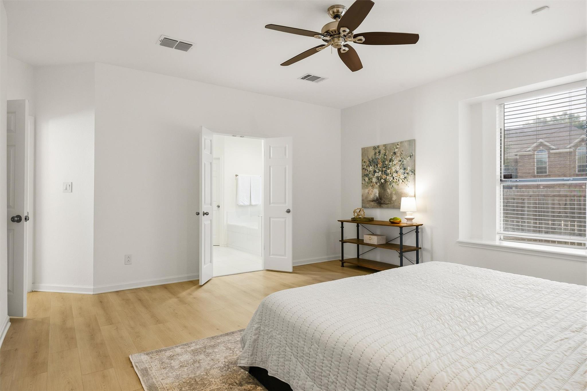 Bedroom with a white quilted bed, ceiling fan, and open doorway to a bathroom.