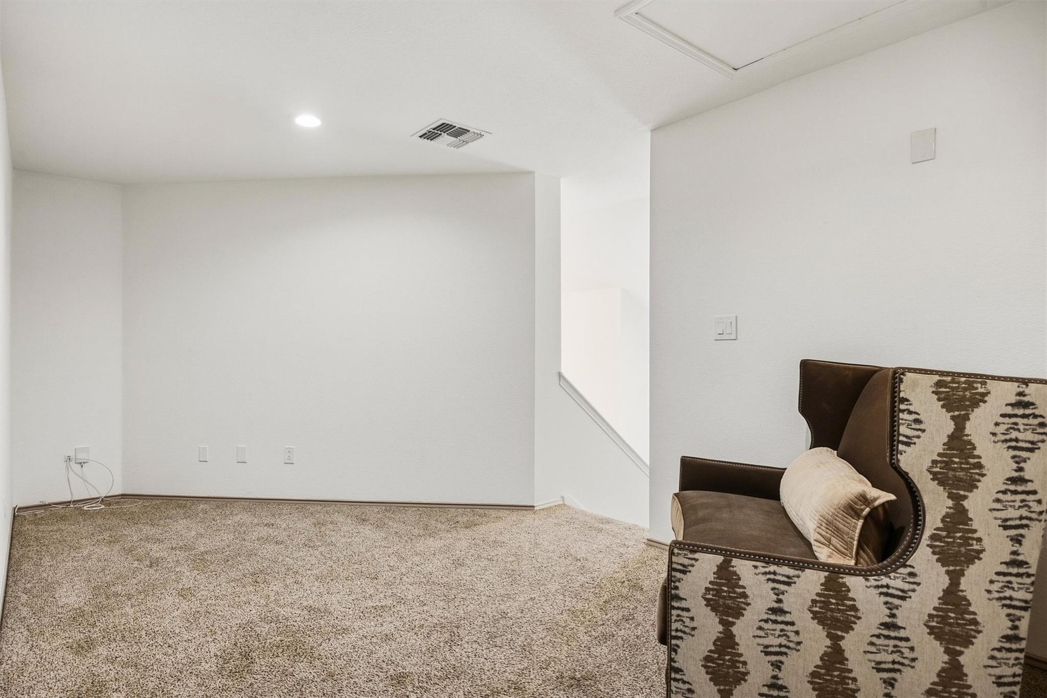 Carpeted room with a patterned chair beside an open stairway.