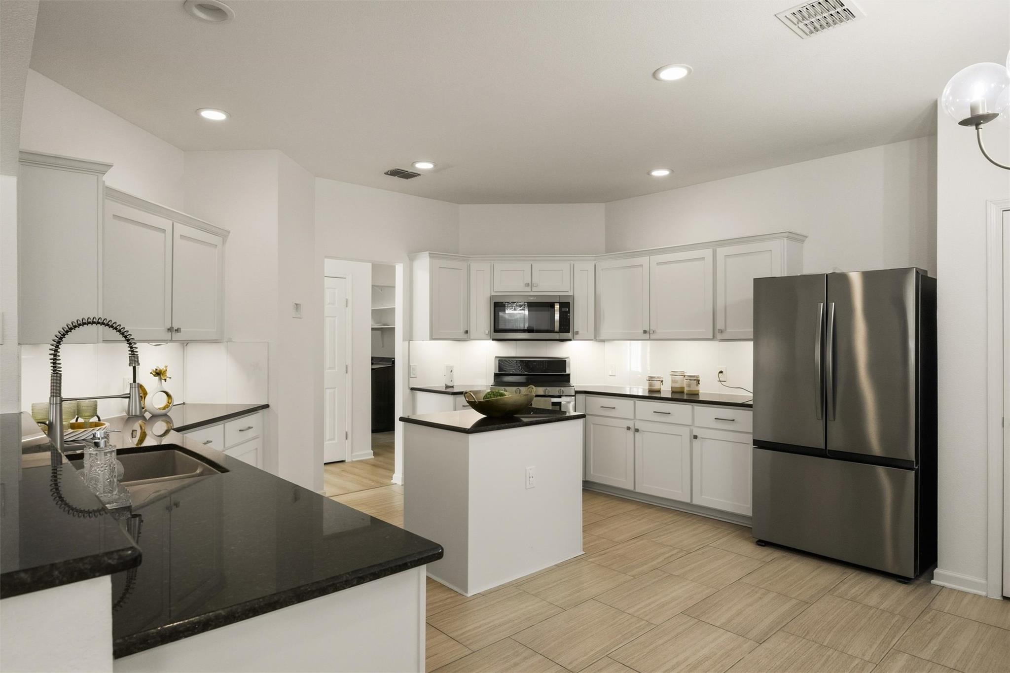 Kitchen with white cabinets, black countertops, a central island, and stainless steel appliances.